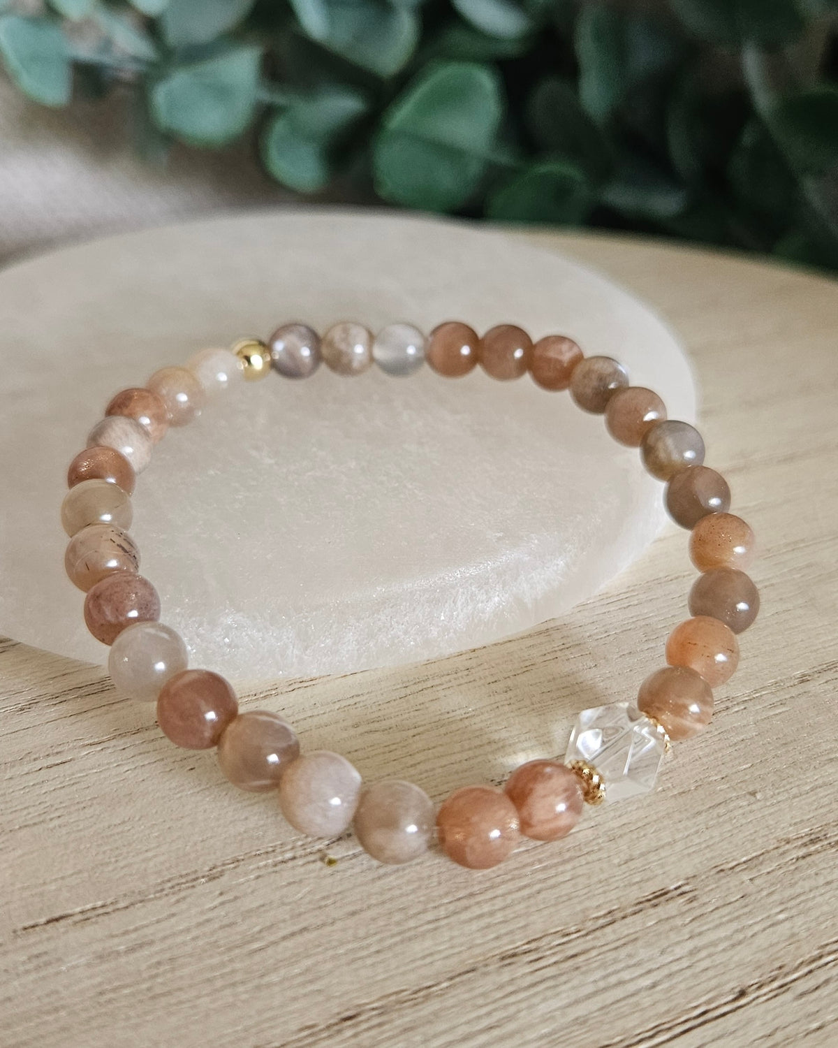 Chocolate Moonstone Still bracelet with 6mm warm neutral gemstone beads, Clear Quartz focal and gold accents styled on selenite with greenery behind it