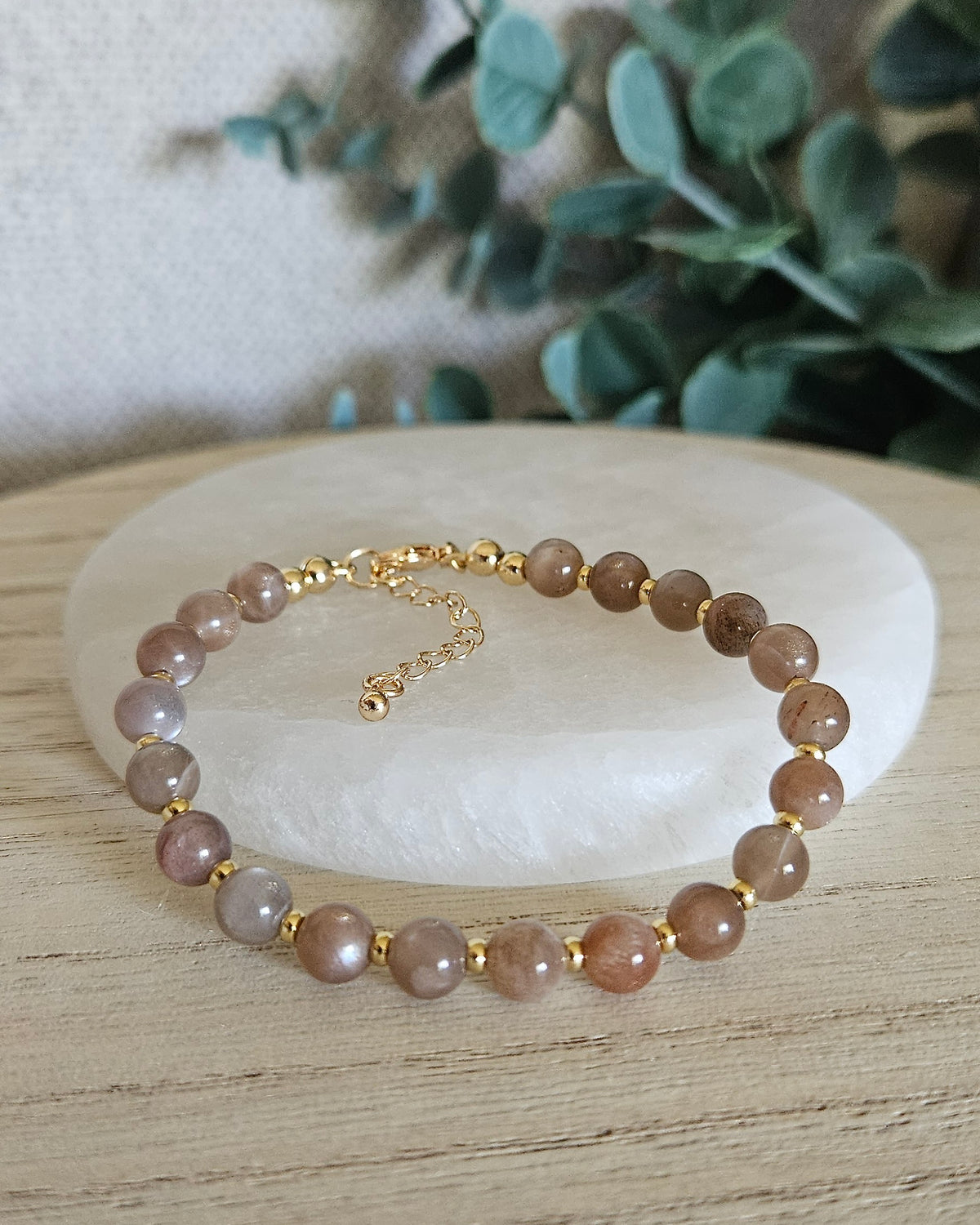 Chocolate Moonstone Echo bracelet with 6mm neutral gemstone beads, 14k gold-plated accents and extender chain styled on selenite with greenery