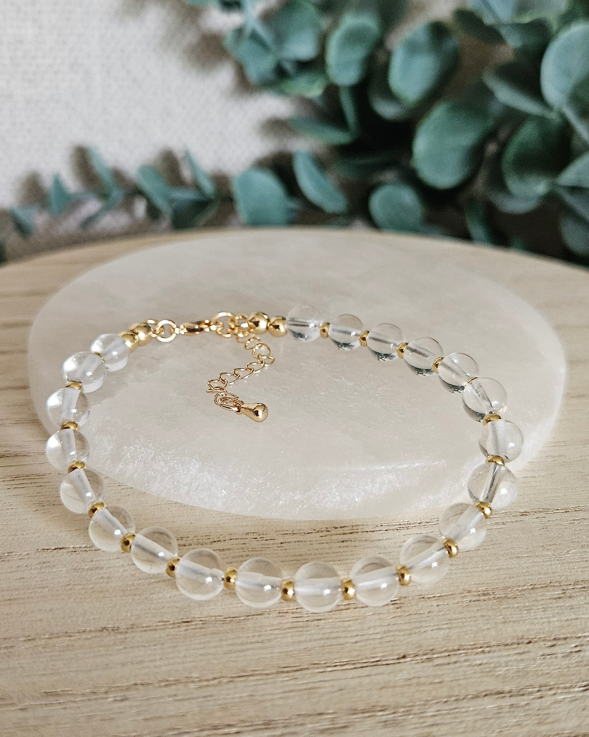 Clear Quartz Echo bracelet with transparent 6mm gemstone beads, gold-plated accents, clasp and extender chain styled on selenite