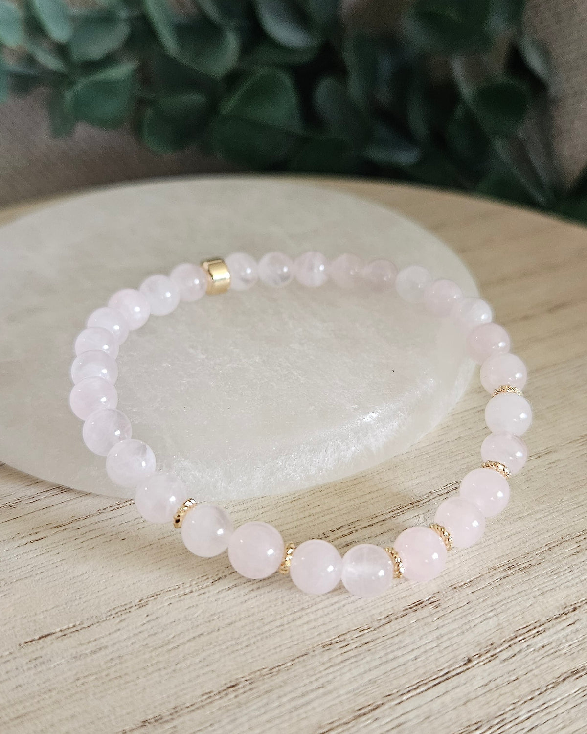 Rose Quartz Grace bracelet with 6mm soft pink gemstone beads and gold-plated accents styled on selenite with greenery behind it