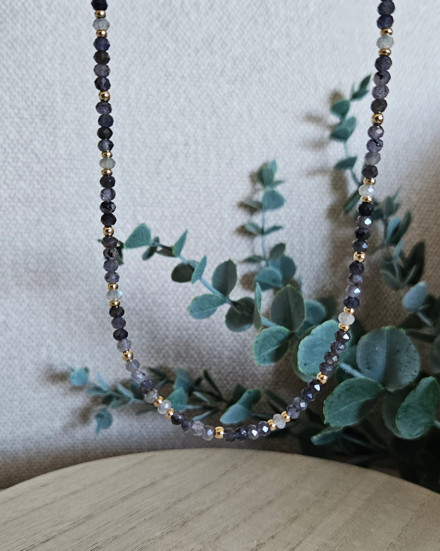 Iolite and Labradorite necklace suspended against eucalyptus greenery, showing its alternating gemstone pattern