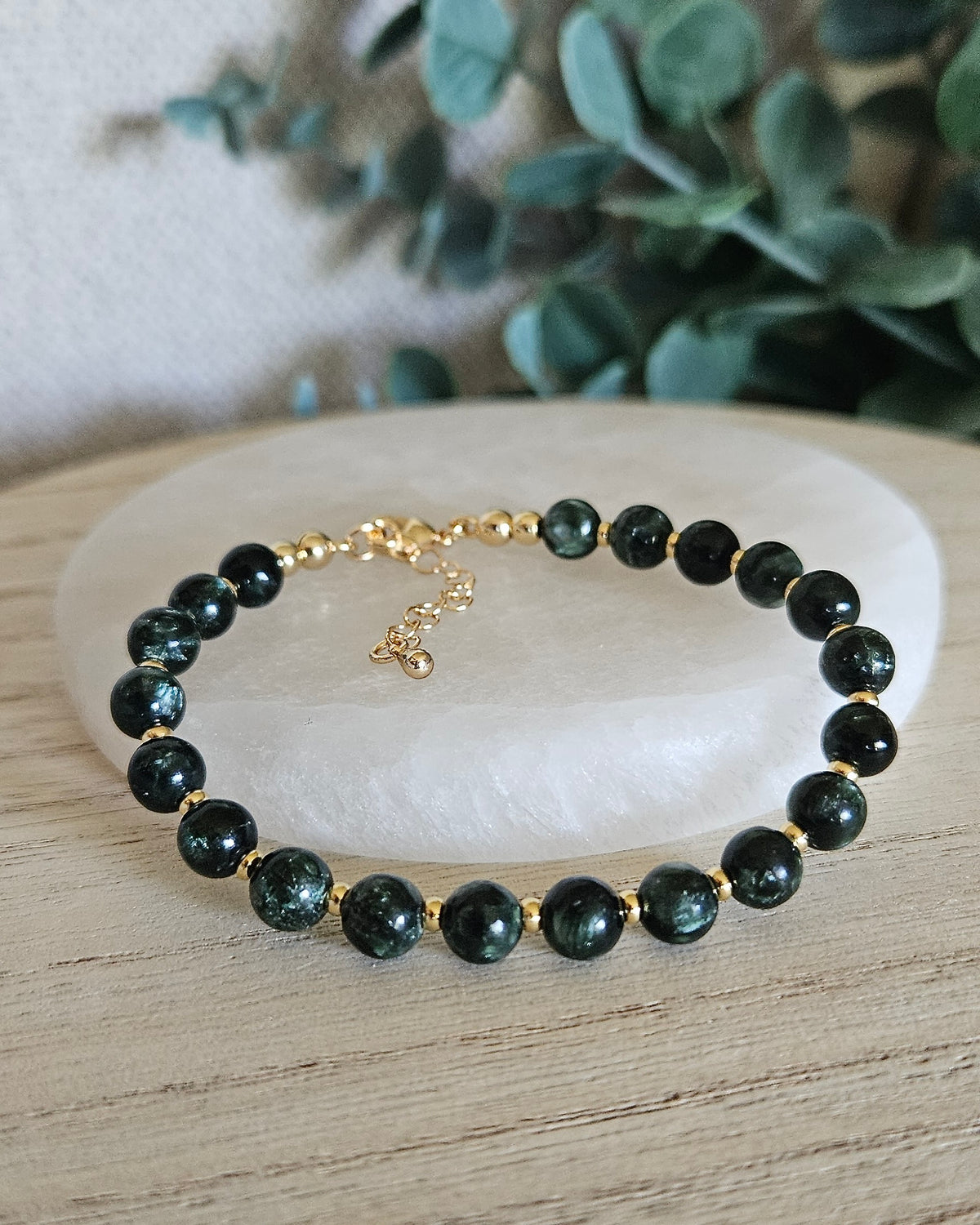 Seraphinite Echo bracelet with 6mm deep green beads, gold-plated accents, clasp and extender chain styled on selenite with greenery
