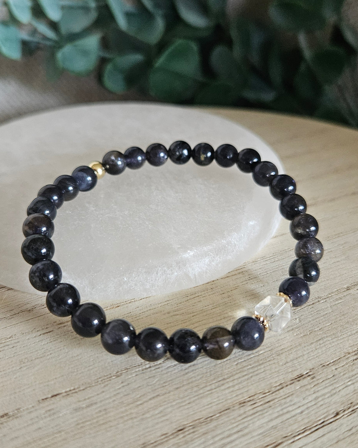 Detailed view of Iolite beads with a Clear Quartz hexagon focal and 14k gold-plated spacers on a white selenite display