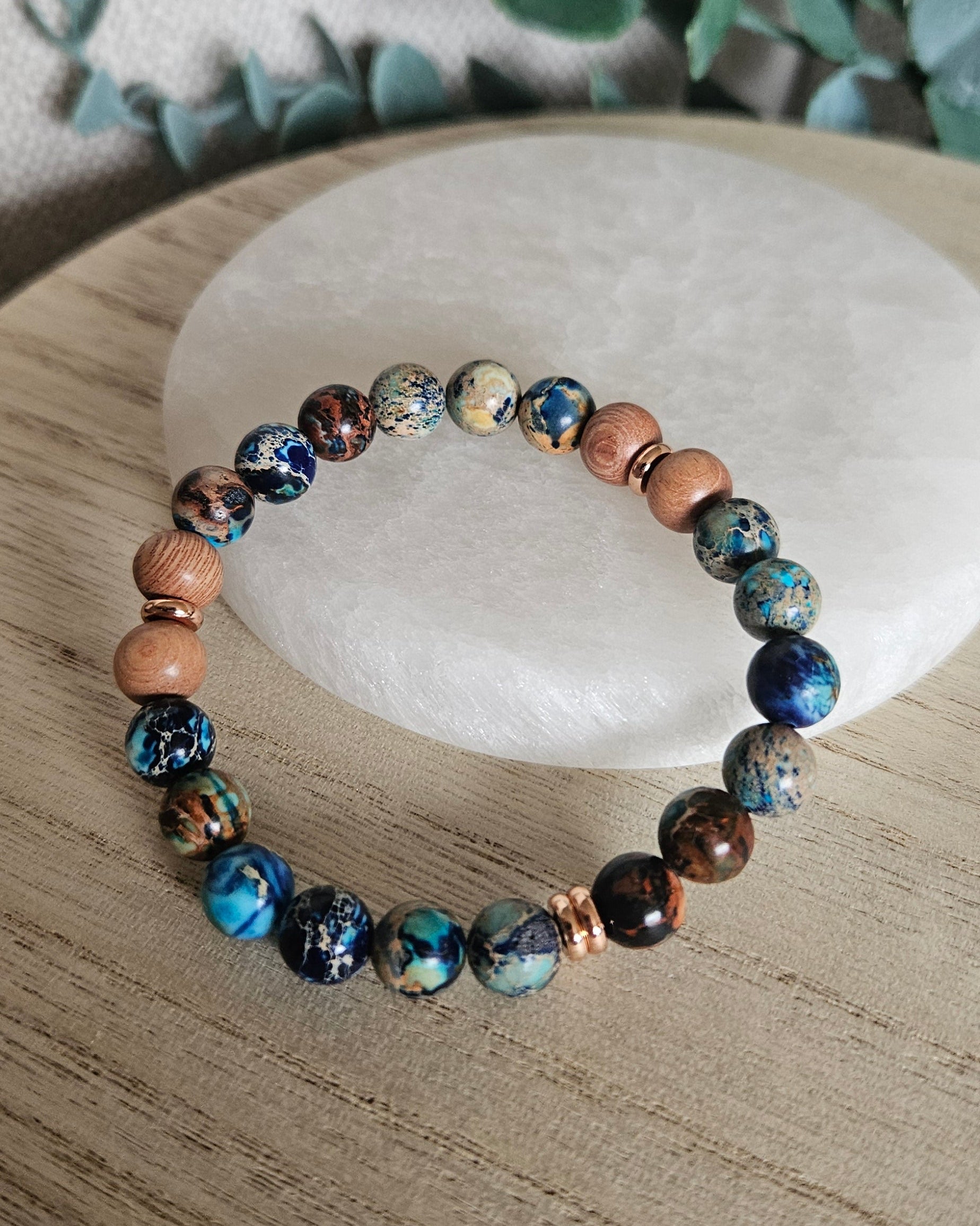 Ocean Blue Sea Sediment Jasper and Rosewood diffuser bracelet with rose gold-plated accents on a pale stone tray