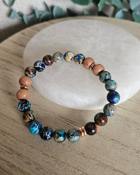 Ocean Blue Sea Sediment Jasper and Rosewood diffuser bracelet with rose gold-plated accents on a pale stone tray