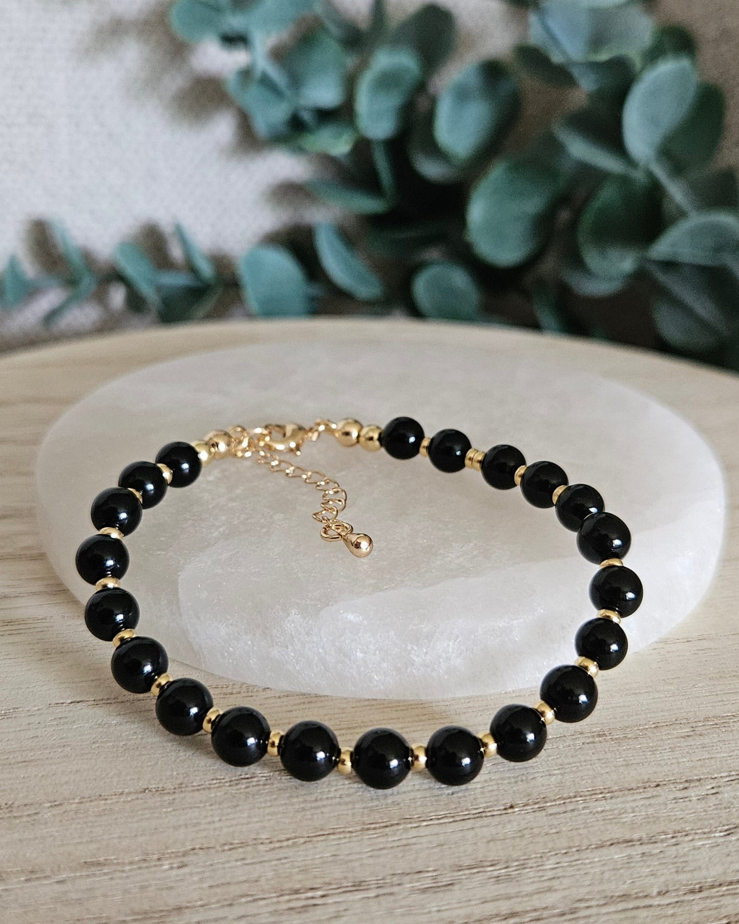 Black Onyx Echo bracelet arranged before a selenite plate with eucalyptus in the background