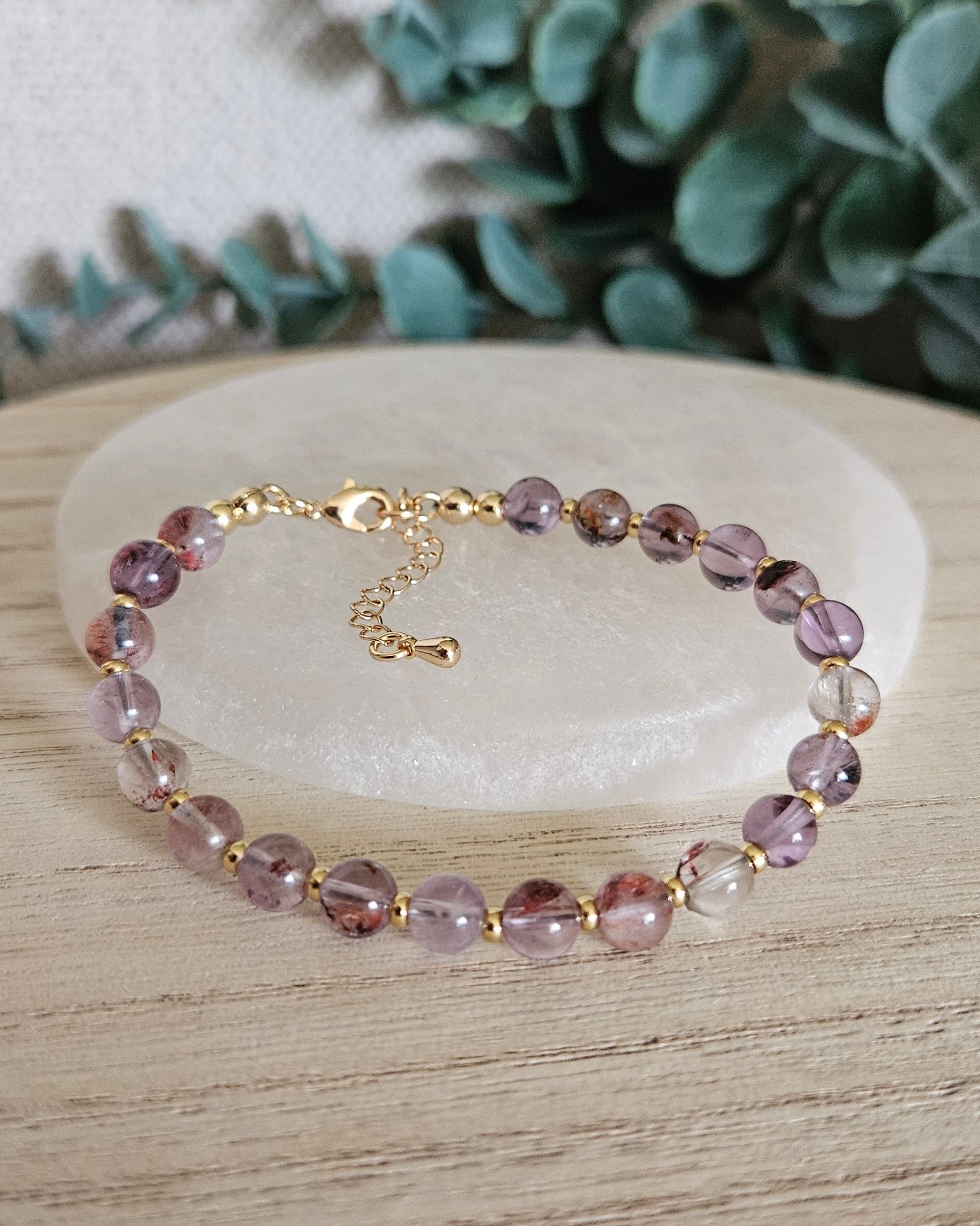 Super Seven Echo bracelet arranged before a selenite plate with eucalyptus in the background