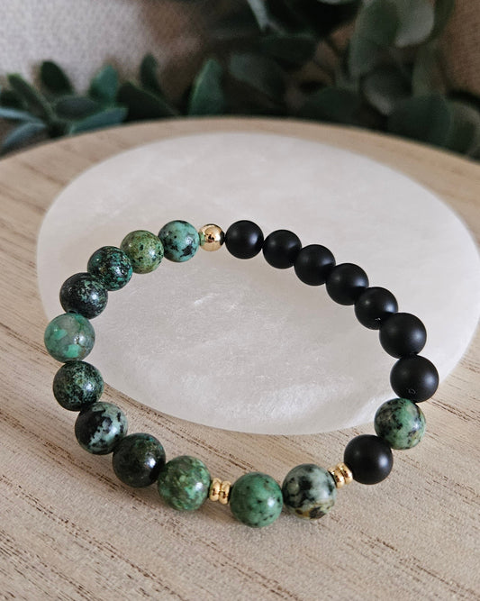 African Turquoise and matte Black Onyx stretch bracelet with gold-plated accents displayed beside a round selenite plate