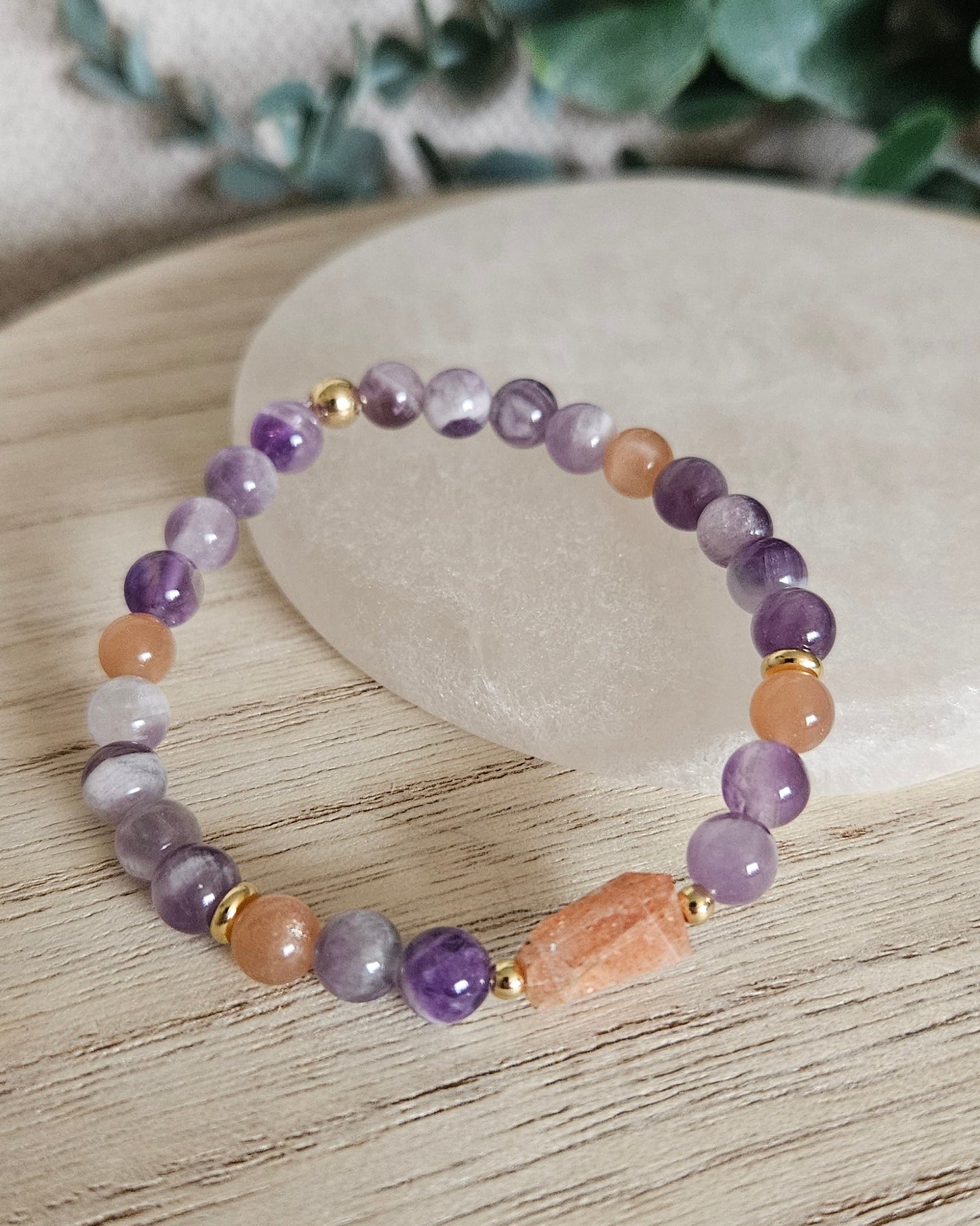 Amethyst and Sunstone bracelet arranged before a round selenite plate with eucalyptus in the background