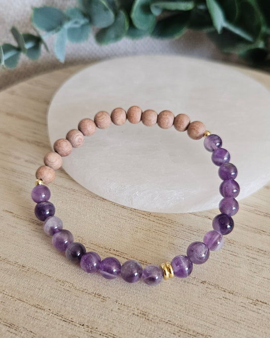 Amethyst and unwaxed Rosewood diffuser bracelet with gold-plated accents displayed beside a selenite plate