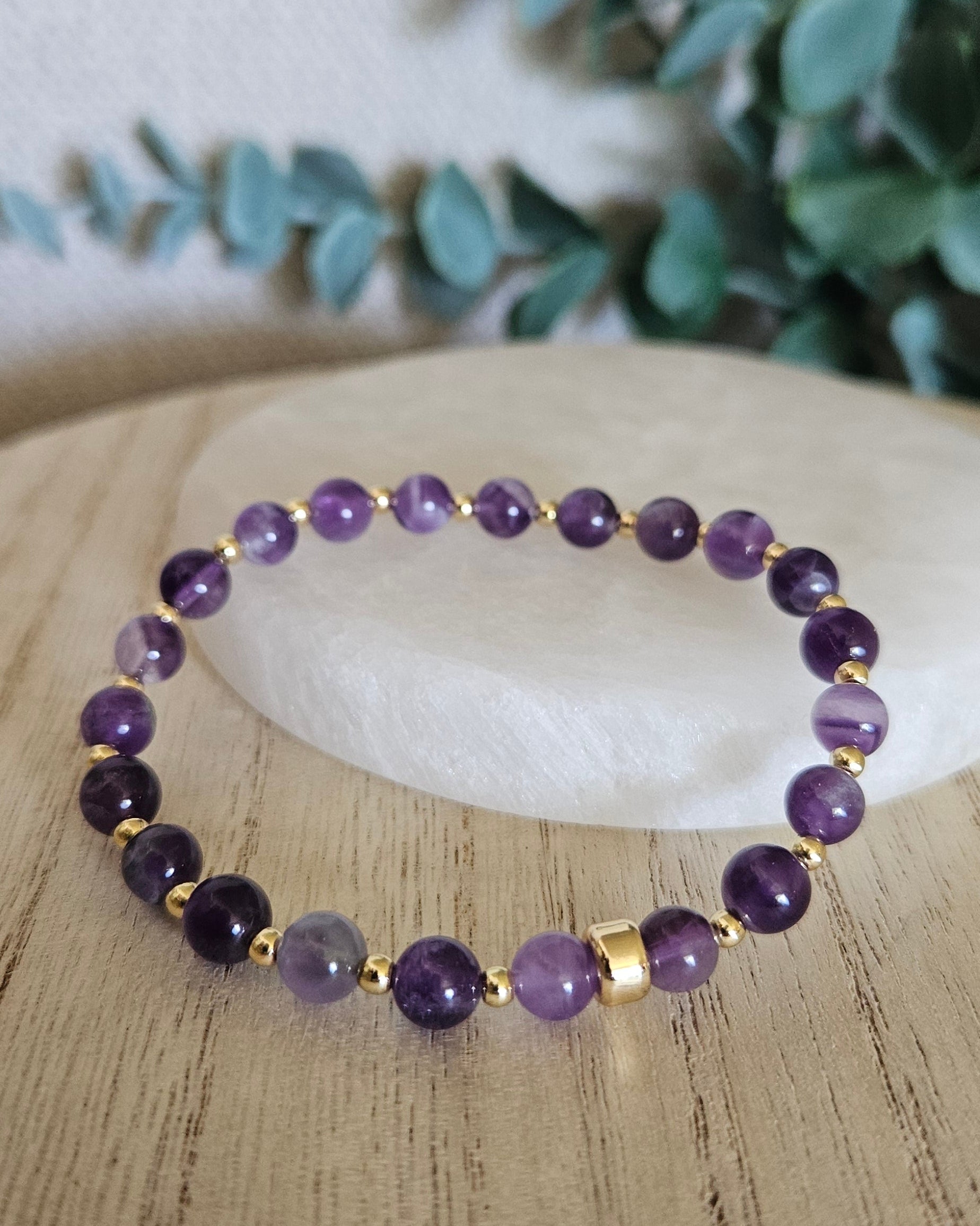 Amethyst bracelet arranged before a round selenite plate with eucalyptus in the background