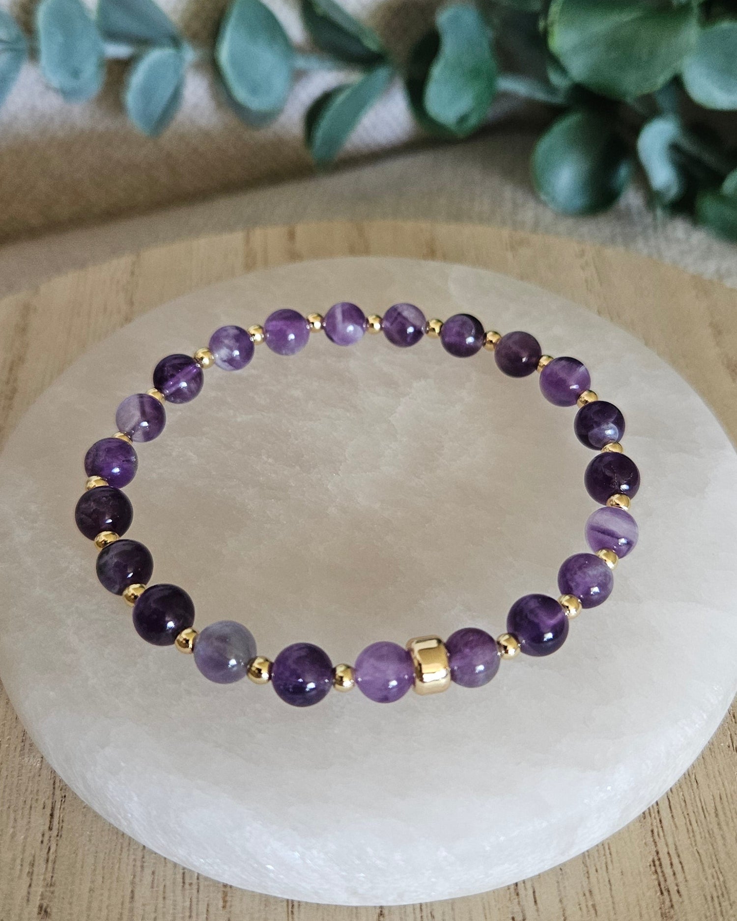 Purple beaded bracelet on a wooden coaster with green leaves in the background