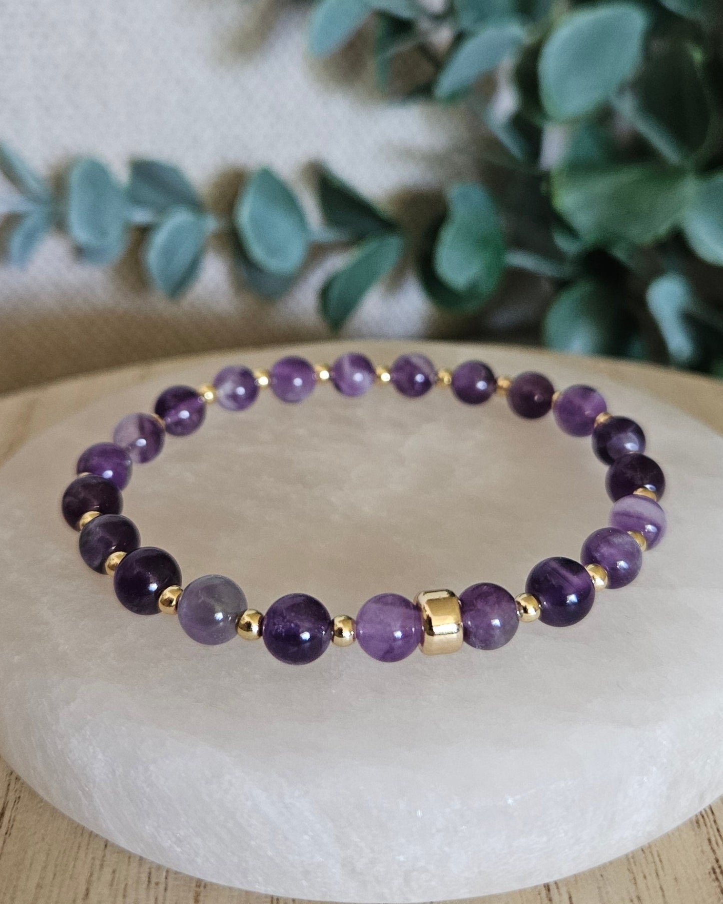 Amethyst stretch bracelet with gold-plated spacer beads and focal accent displayed on a round selenite plate