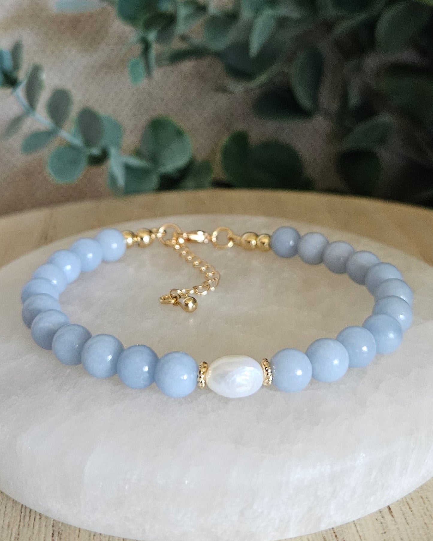 Angelite Embrace bracelet with freshwater pearl focal and gold-plated accents displayed on a selenite plate