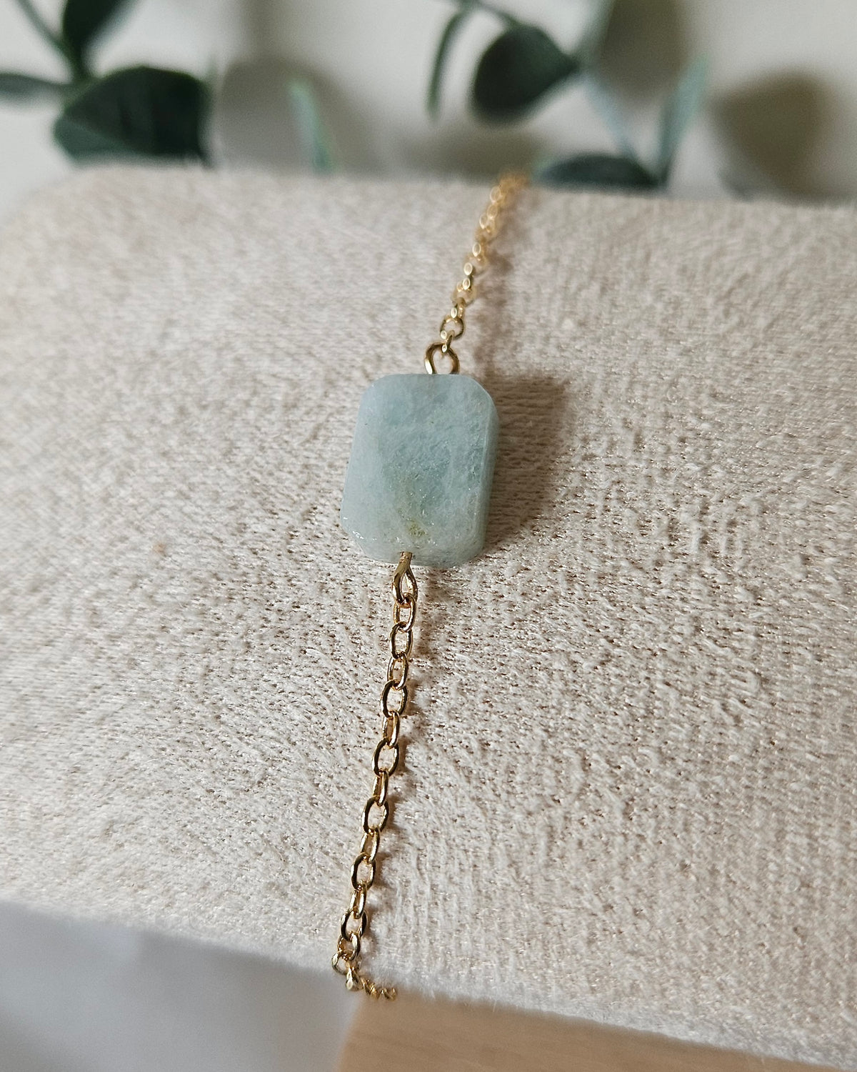 Aquamarine Whisper bracelet with a soft blue rectangular gemstone focal on a delicate 14k gold-plated chain displayed on a textured bracelet stand