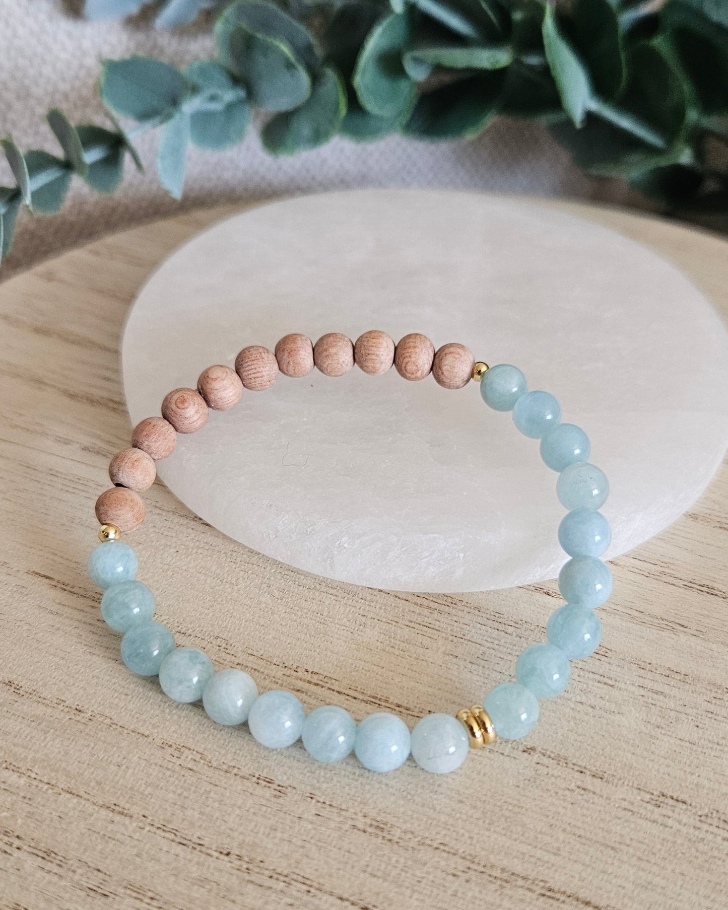 Aquamarine and unwaxed Rosewood diffuser bracelet with gold-plated accents displayed beside a selenite plate