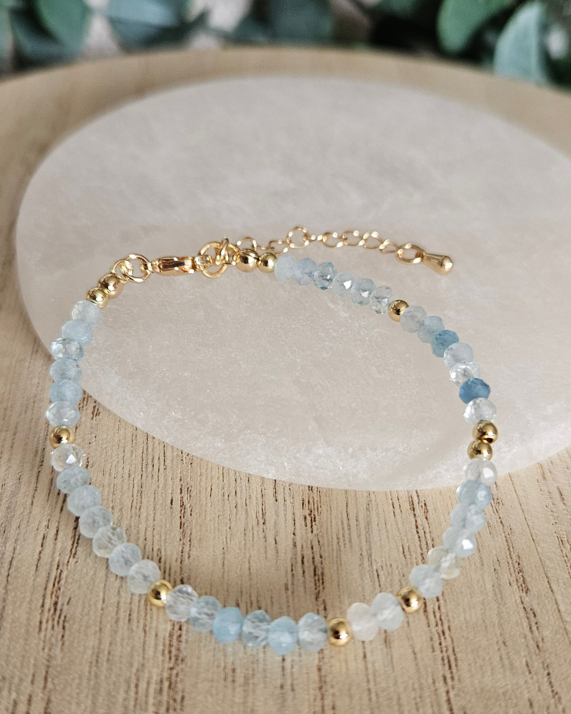 Aquamarine rondelle bracelet arranged before a round selenite plate with eucalyptus in the background