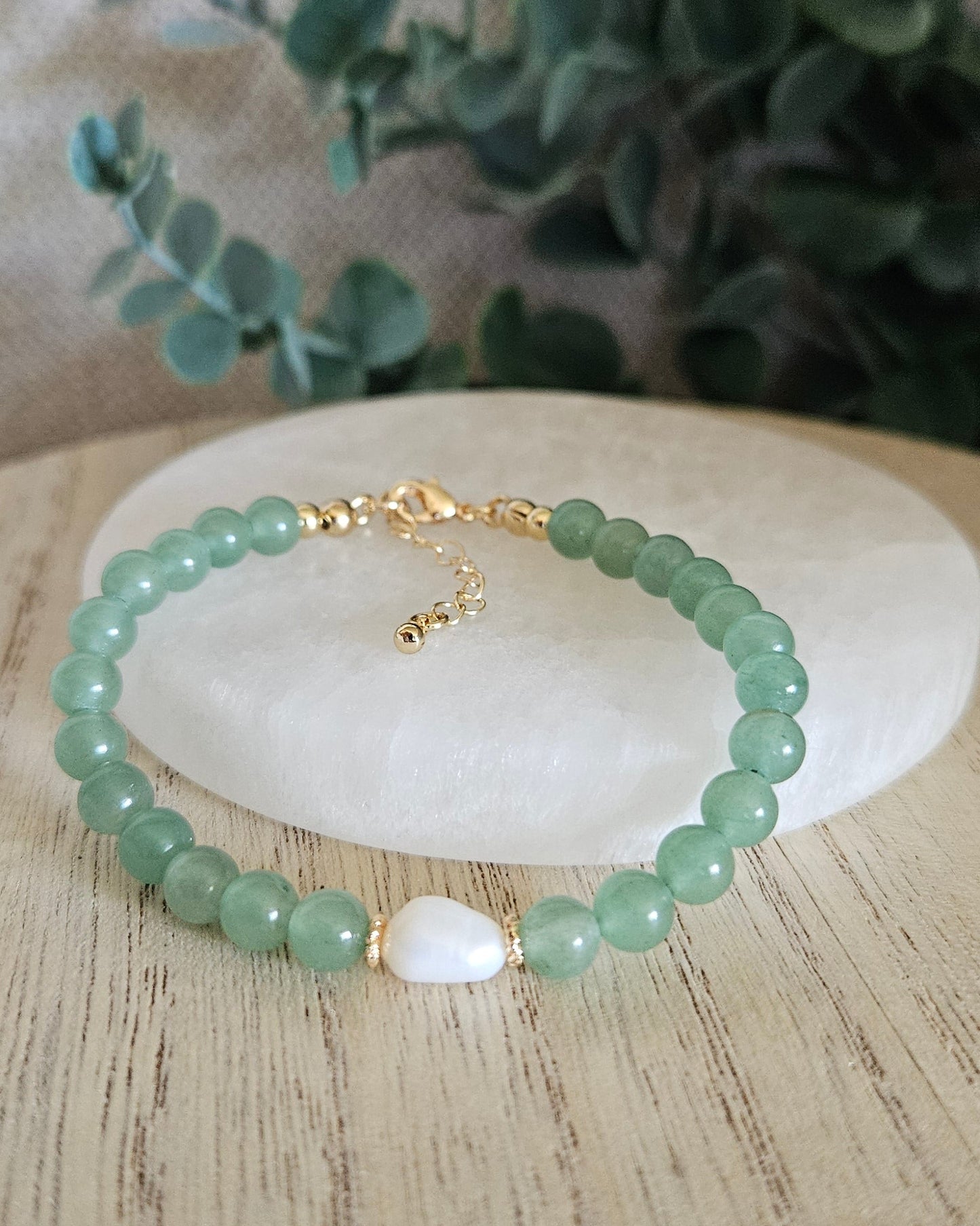 Green Aventurine Embrace bracelet arranged before a selenite plate with a freshwater pearl focal and eucalyptus background