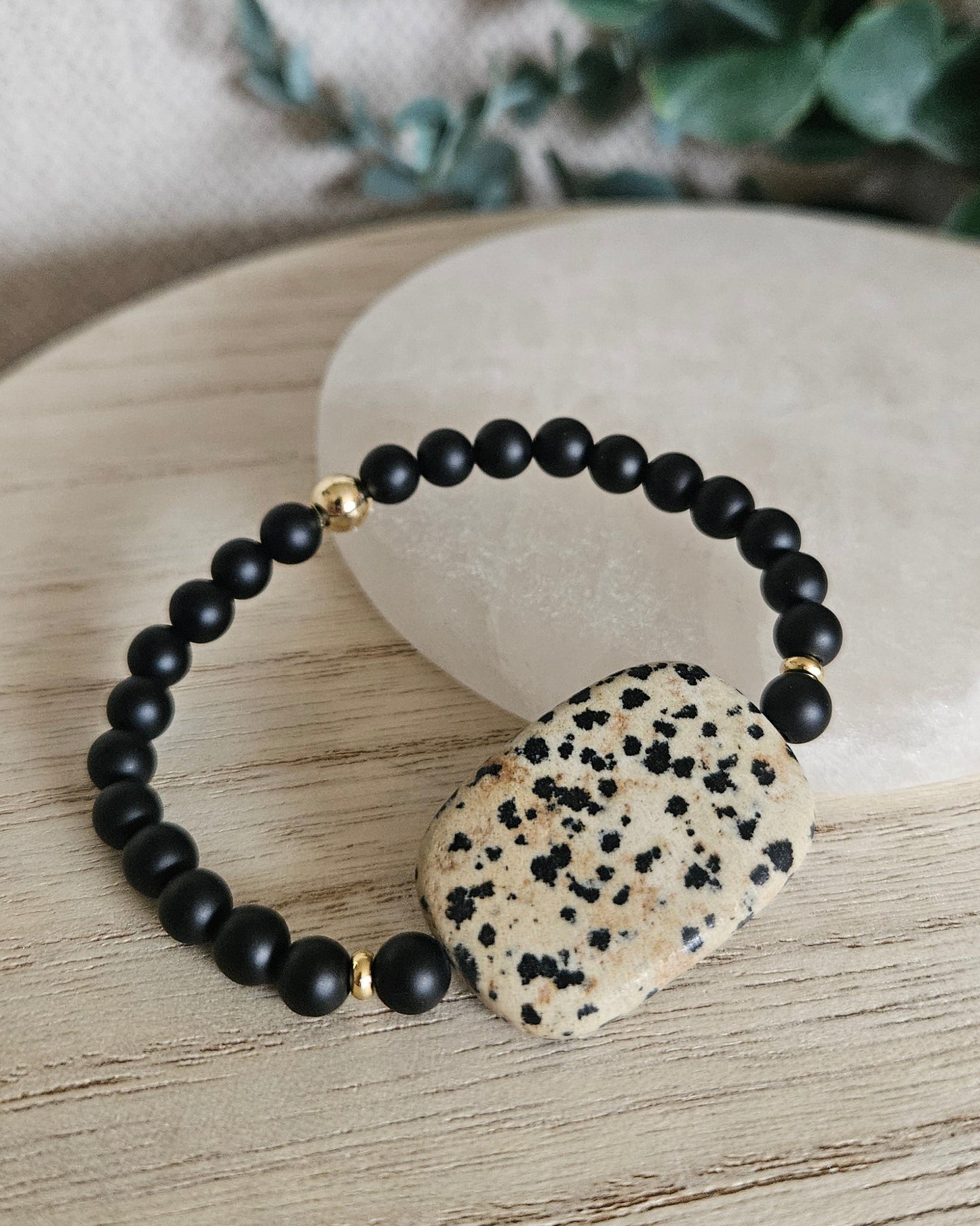 Black Onyx and Dalmatian Jasper bracelet arranged before a round selenite plate on a wooden surface