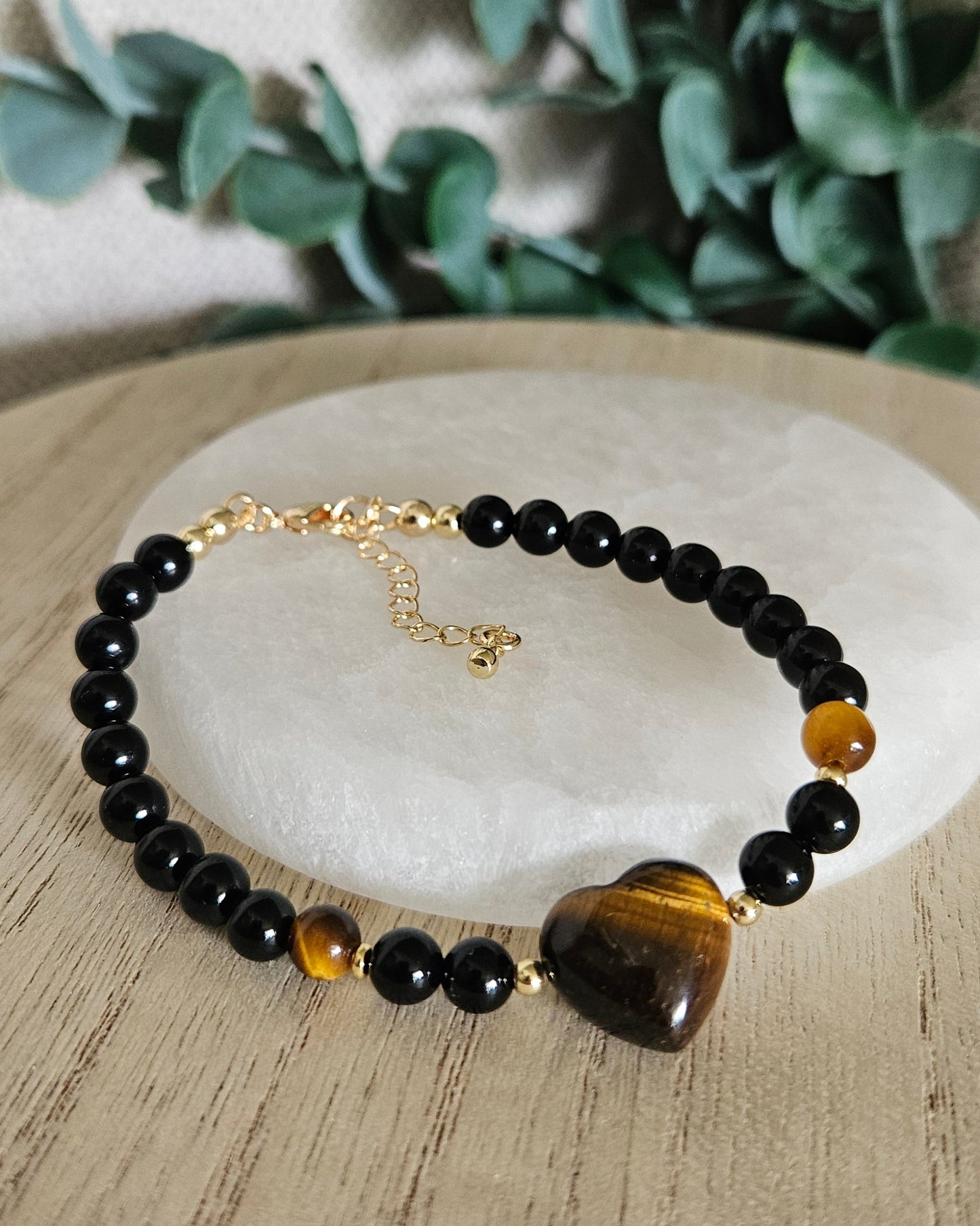 Black Onyx and Tiger's Eye heart bracelet arranged before a round selenite plate with eucalyptus in the background
