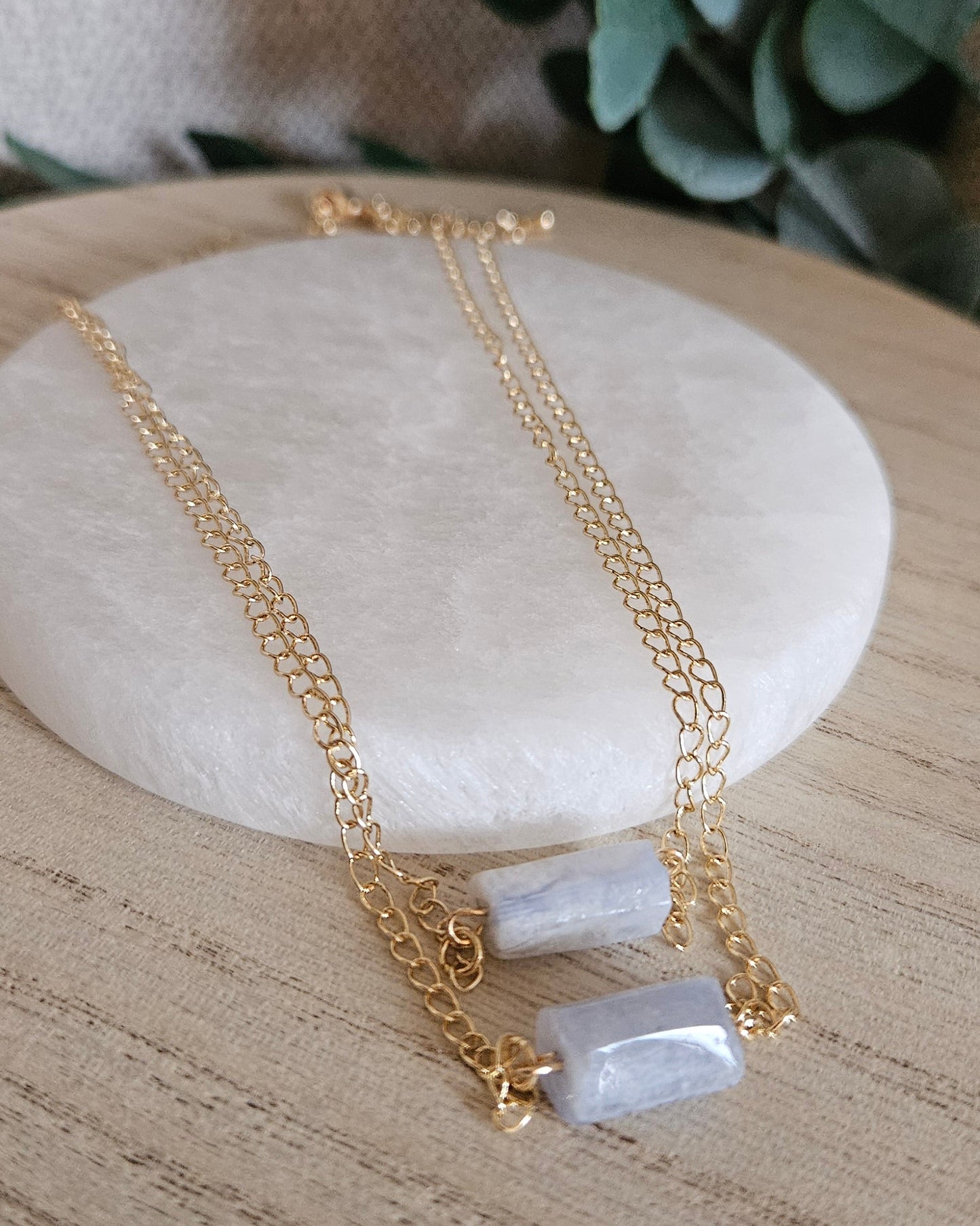 Blue Lace Agate double-chain necklace arranged on light wood beside a round selenite plate