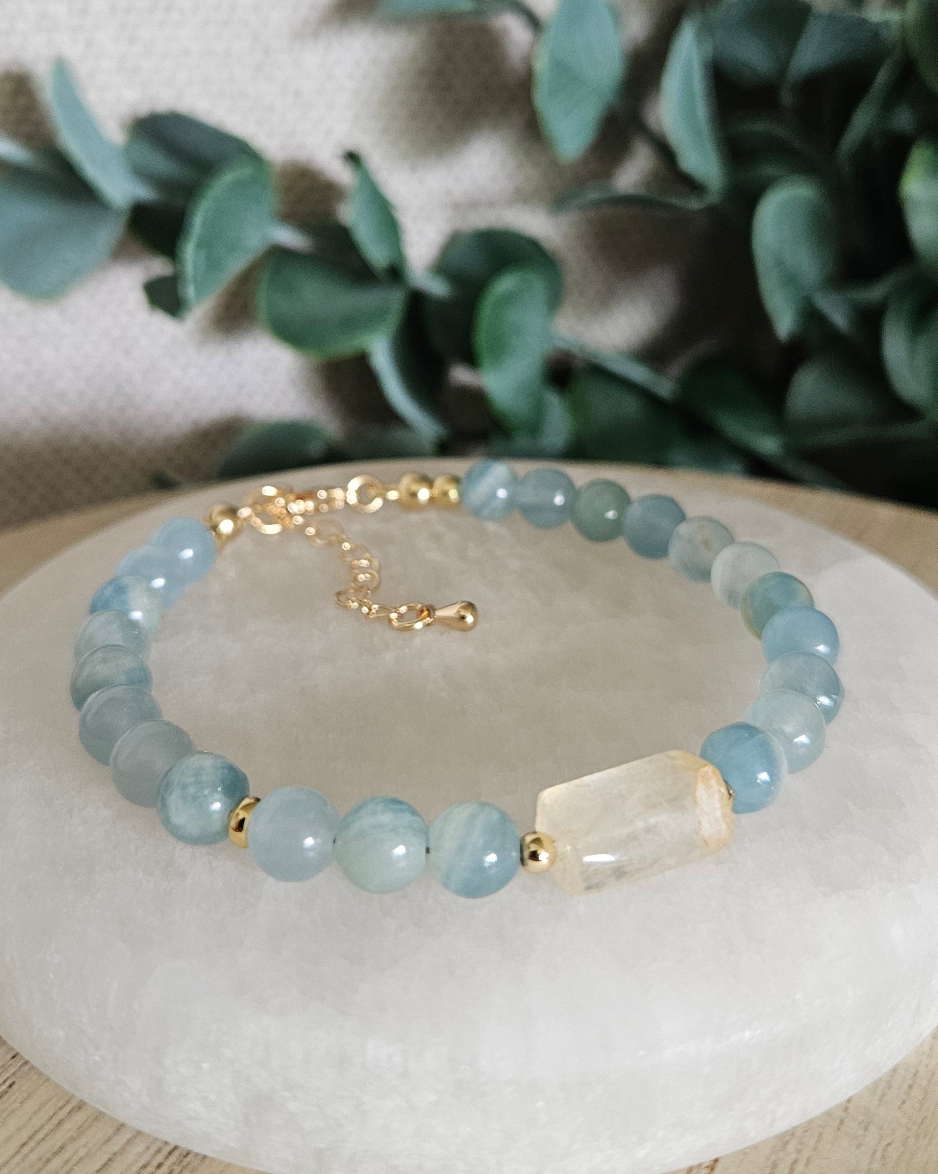 Blue Calcite bracelet with a Citrine barrel focal and gold accents displayed on a round selenite plate