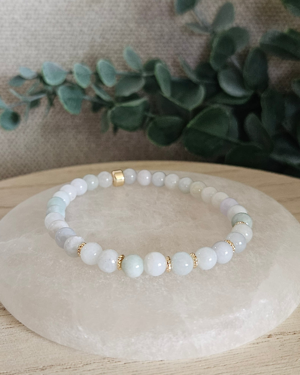 Burmese Jade Grace bracelet with 6mm pale gemstone beads and gold-plated spacer accents on selenite with greenery behind it