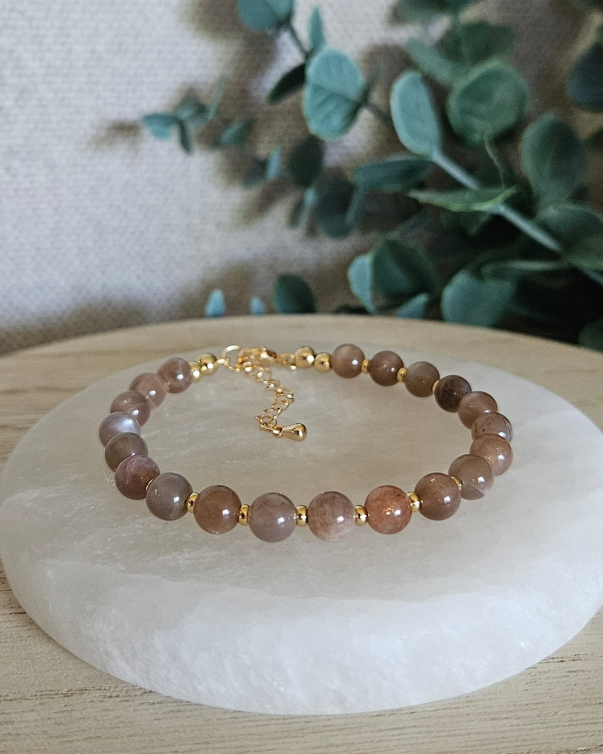 Chocolate Moonstone Echo bracelet with 6mm warm neutral gemstone beads, 14k gold-plated accents, clasp and extender chain displayed on selenite