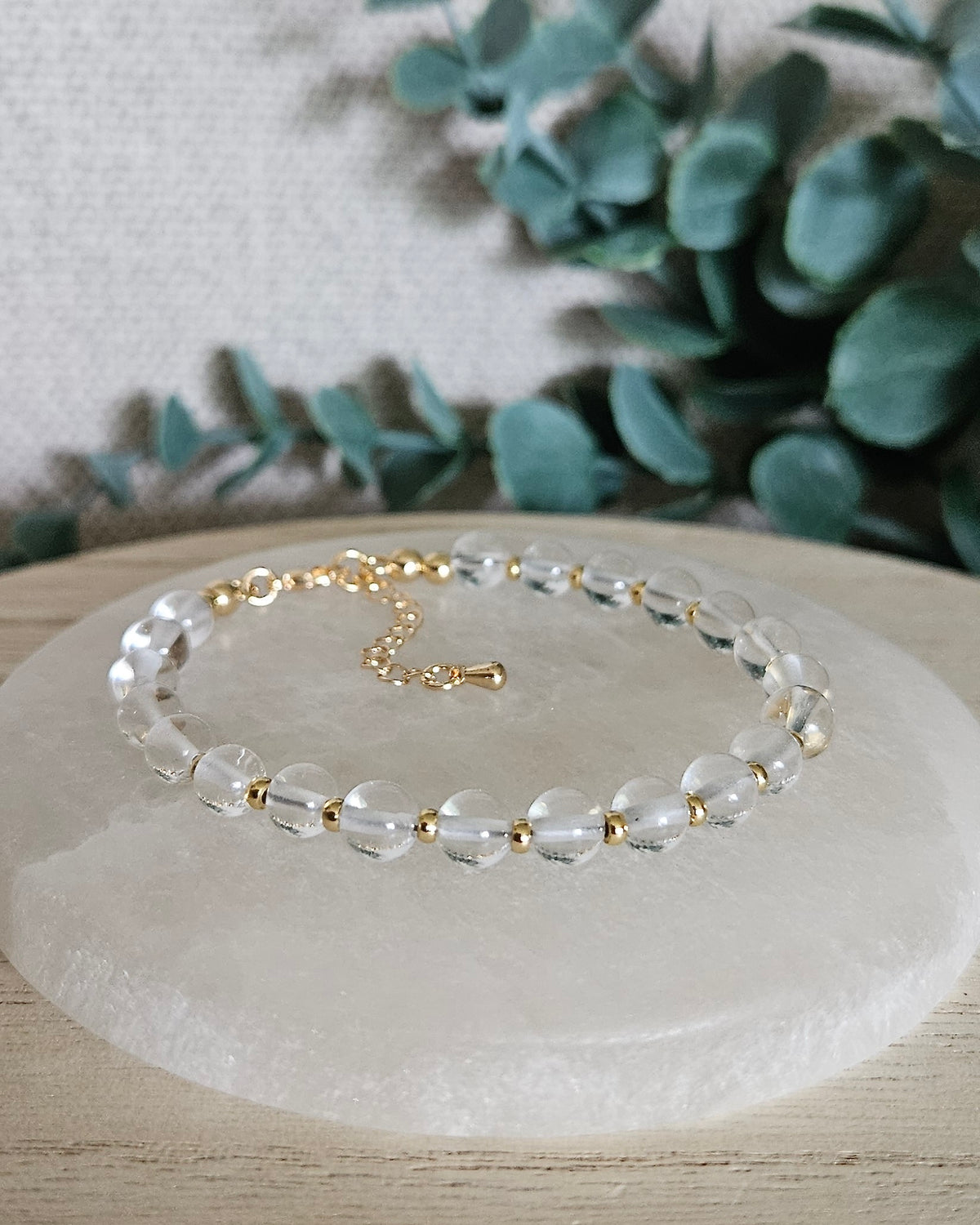 Clear Quartz Echo bracelet with 6mm transparent gemstone beads, 14k gold-plated accents, clasp and extender chain displayed on selenite