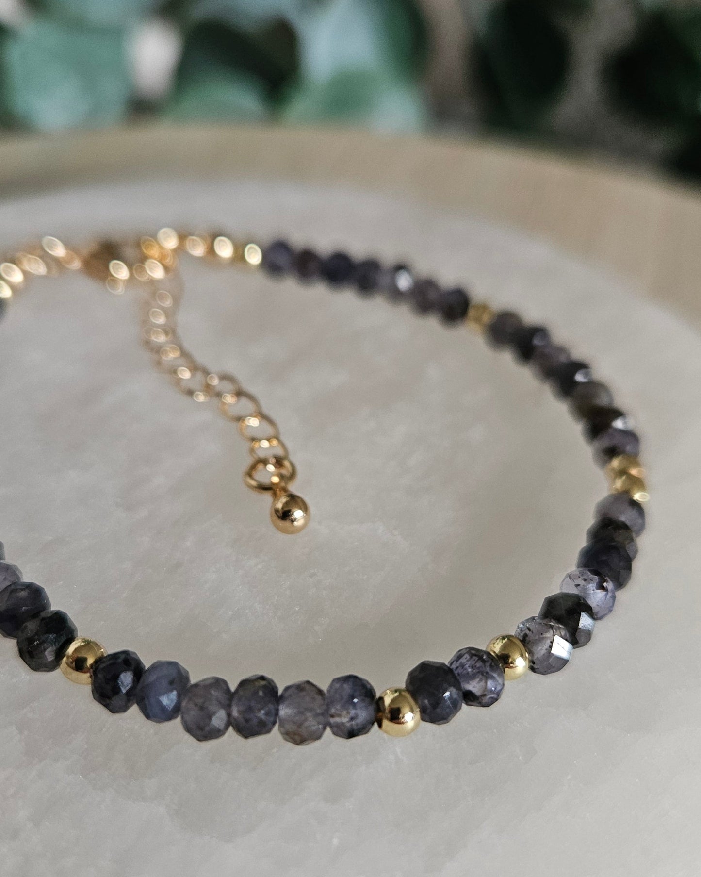 Close-up of the faceted violet-grey Iolite rondelle bracelet with gold-plated accents and extender chain on selenite