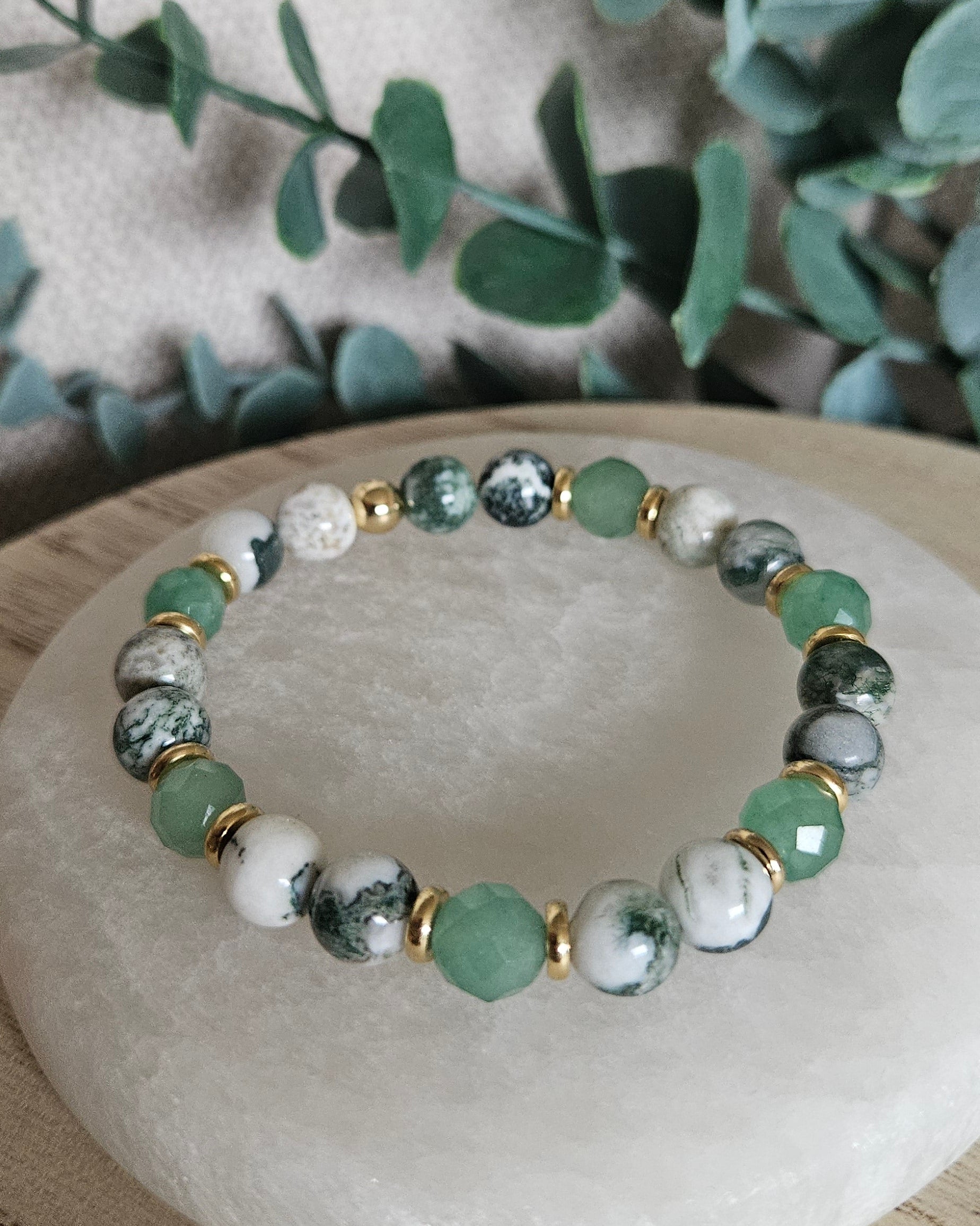 Close-up of Green Aventurine and Tree Agate bracelet with gold-plated accents beside leafy greenery