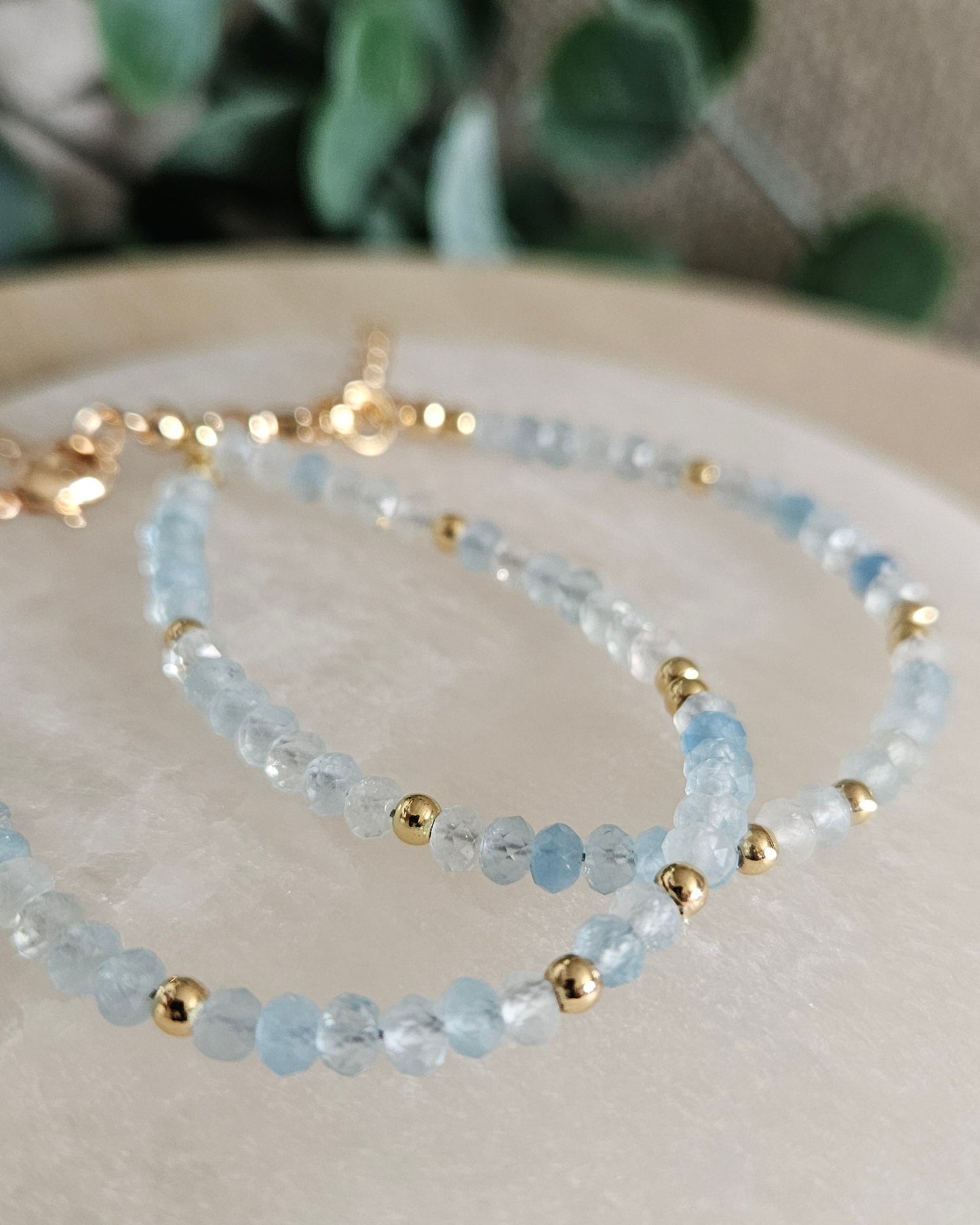 Close-up of two layered Aquamarine rondelle bracelets with gold-plated spacer beads on a round selenite plate