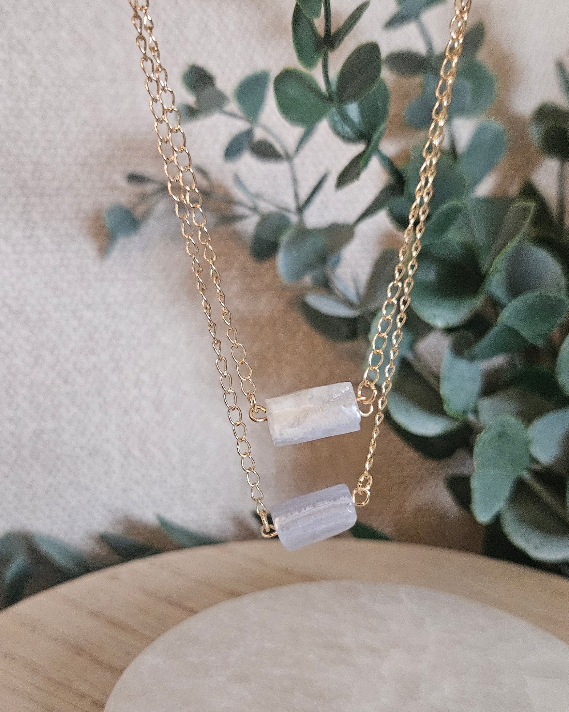 Close angled view of the layered Blue Lace Agate necklace against soft eucalyptus greenery