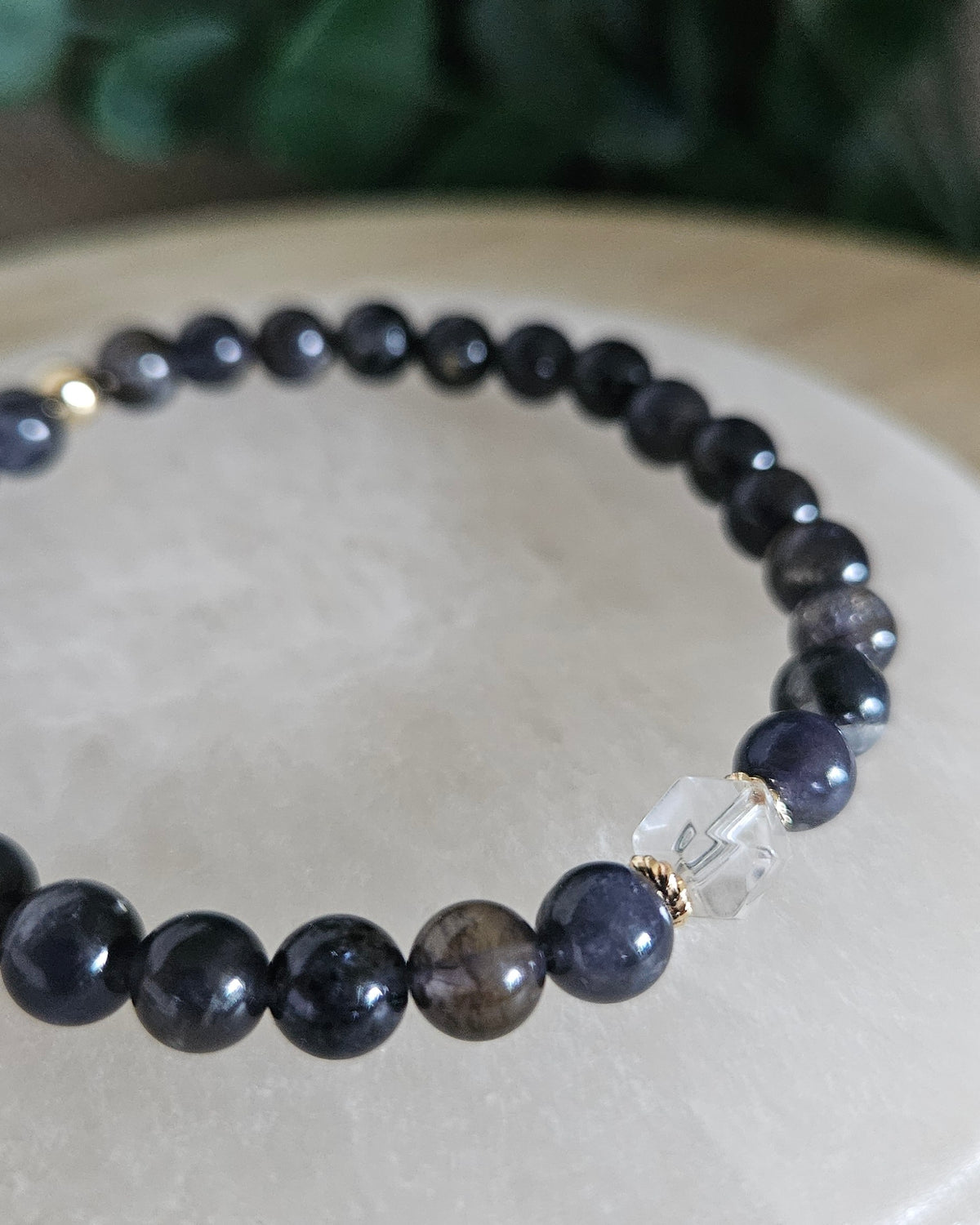 Close view of the Iolite Still bracelet with Clear Quartz hexagon focal, gold-plated accents and dark blue gemstone beads on selenite