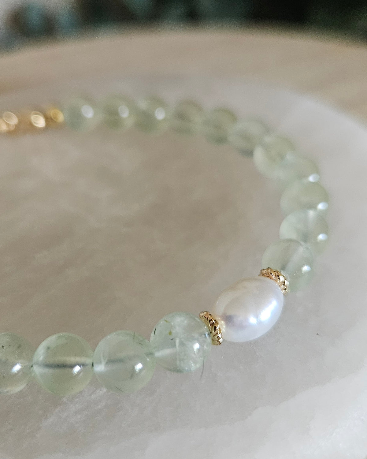 Close view of the Prehnite bracelet showing soft green gemstone beads, freshwater pearl focal and 14k gold-plated spacer accents on selenite