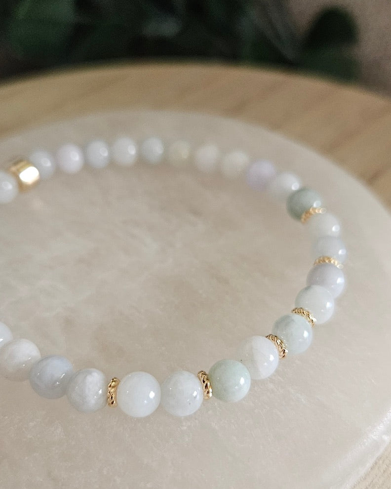 Close view of Burmese Jade beads with soft green, white and pale lavender tones styled on a white selenite display