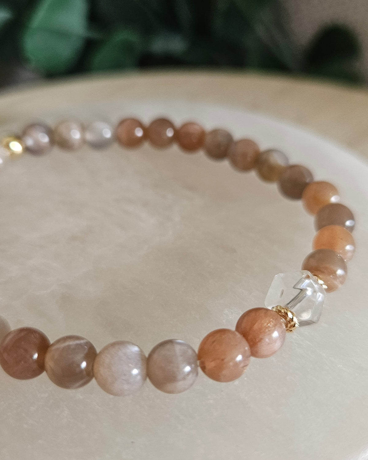 Close view of Chocolate Moonstone beads with peach, cream and brown tones, Clear Quartz hexagon focal and 14k gold-plated spacers on selenite