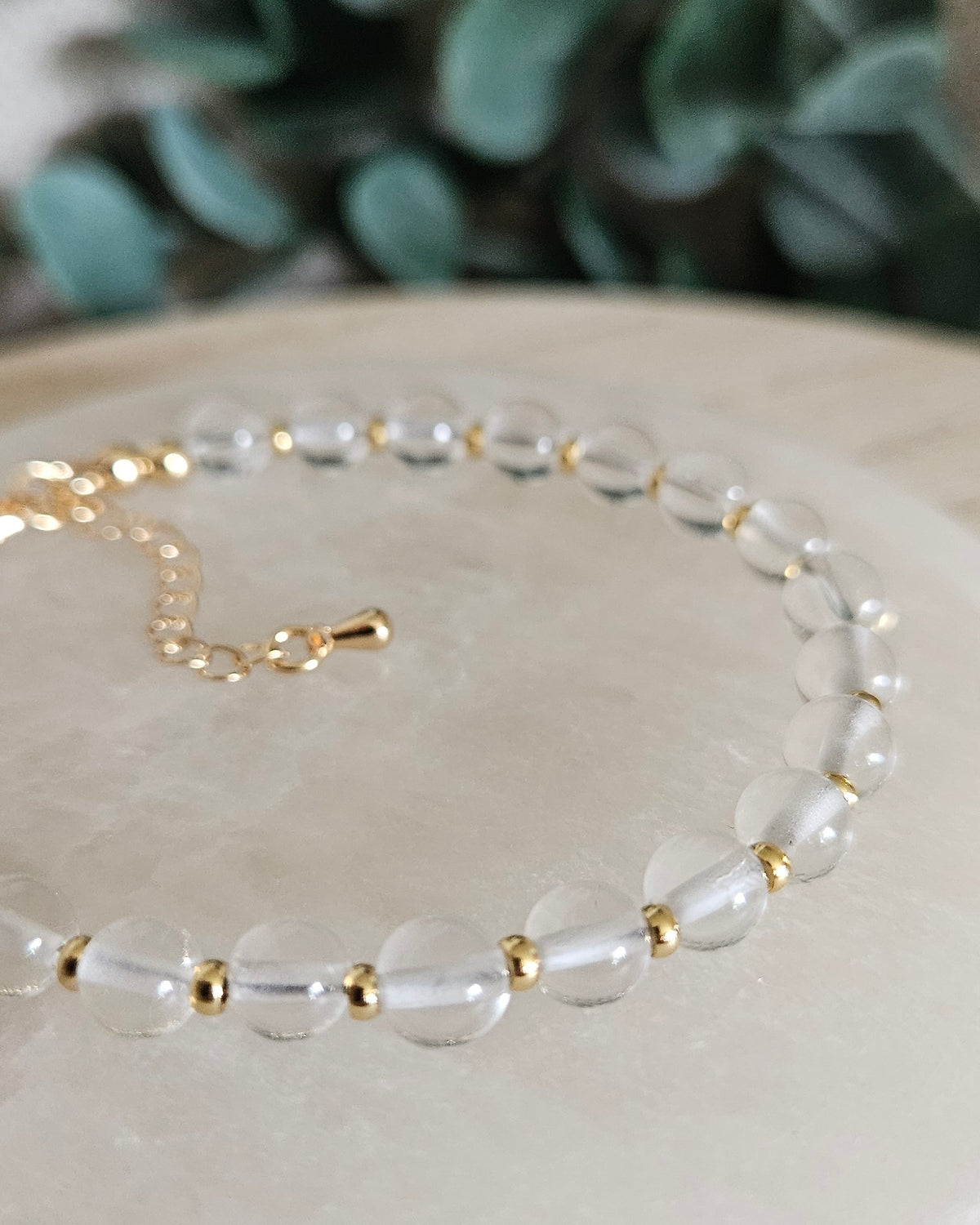 Close view of Clear Quartz beads with 14k gold-plated accent beads and extender chain on a white selenite display