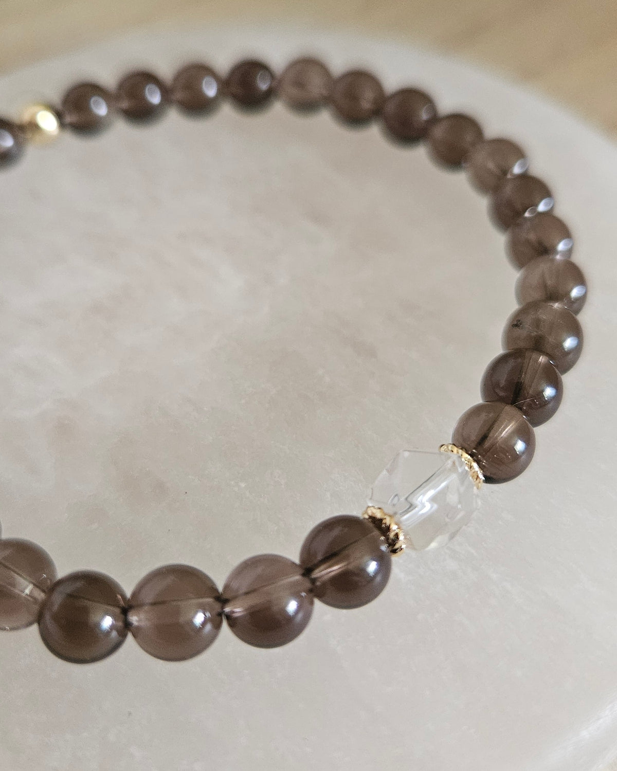 Close view of Smoky Quartz beads with a Clear Quartz hexagon focal and 14k gold-plated spacer accents on selenite