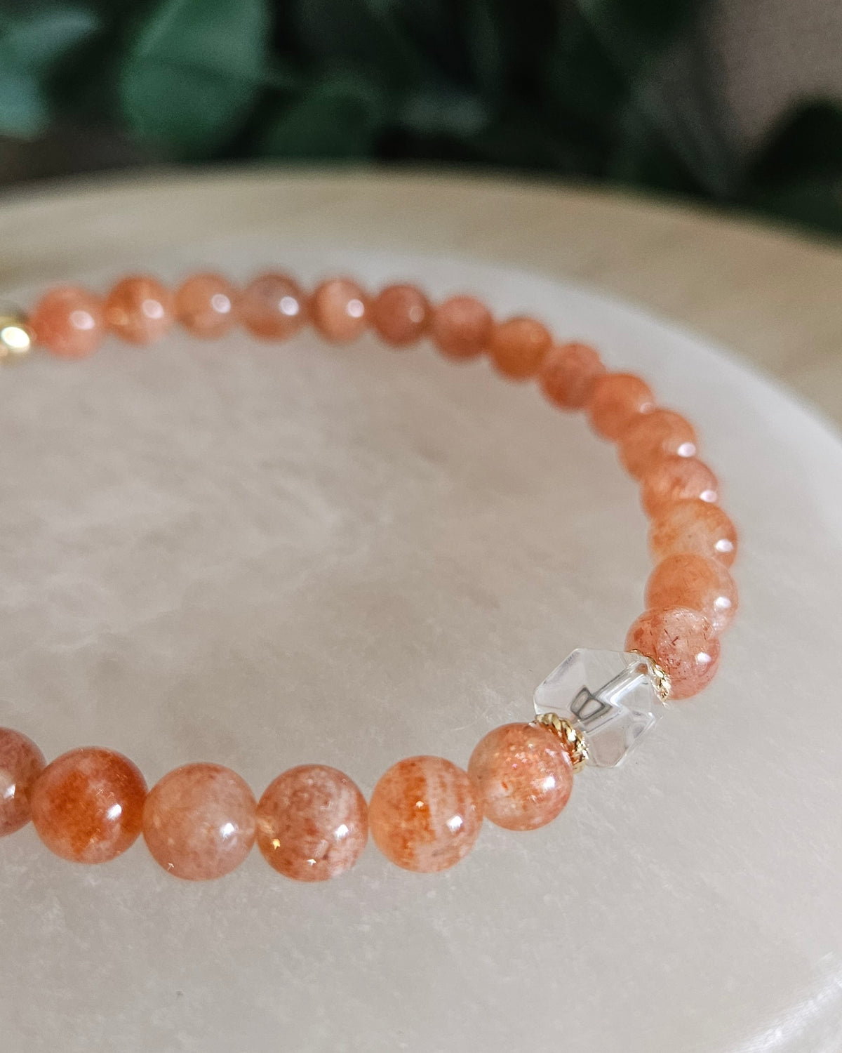 Close view of Sunstone beads with warm orange tones, Clear Quartz hexagon focal and 14k gold-plated spacers on selenite
