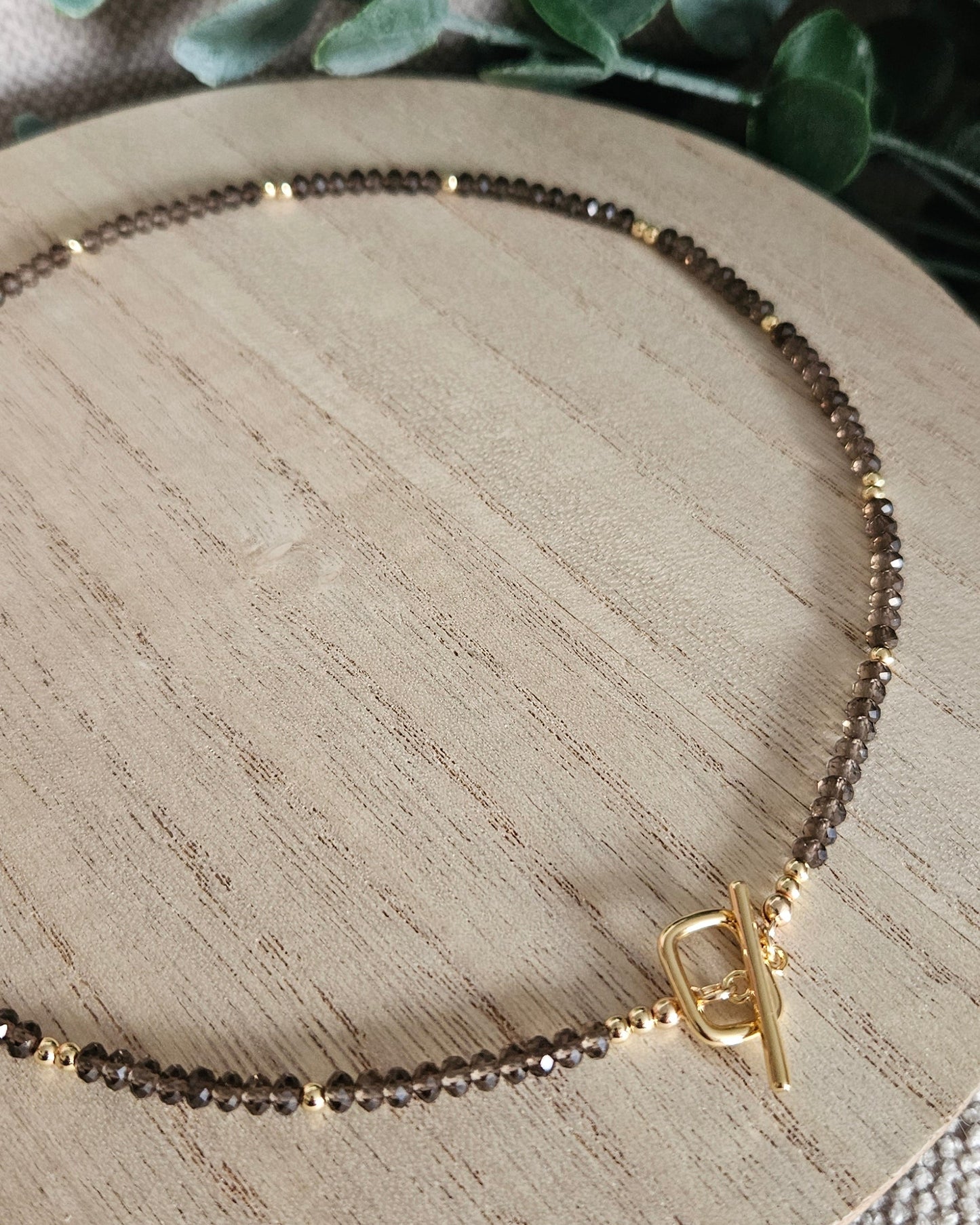 Close view of the faceted Smoky Quartz beads and gold-plated toggle clasp on light wood