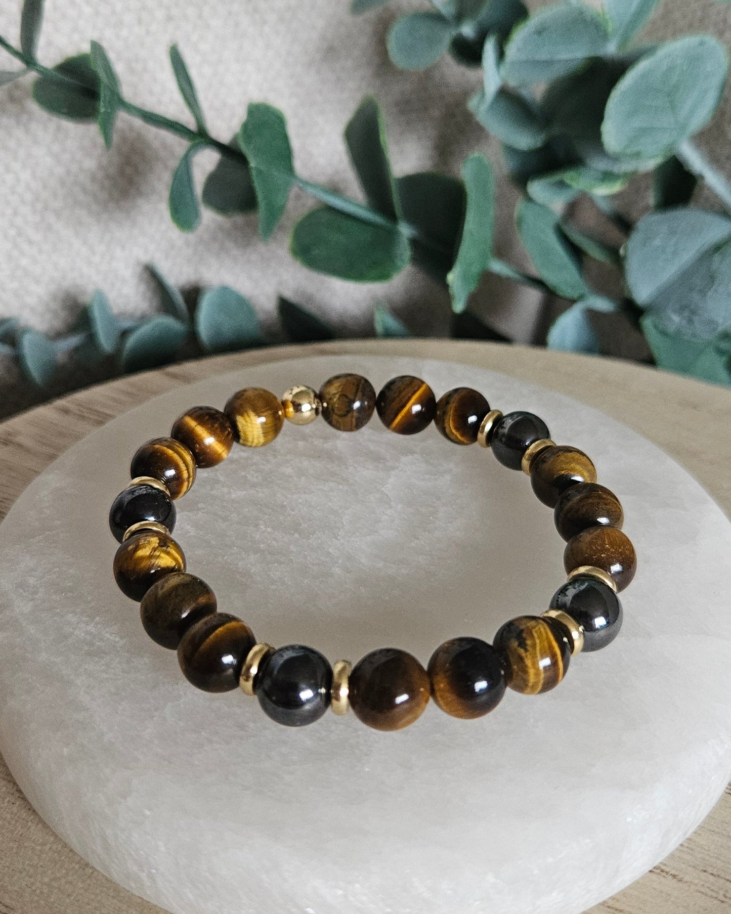 Detailed view of polished Tiger’s Eye and Hematite bracelet beads displayed beside leafy greenery