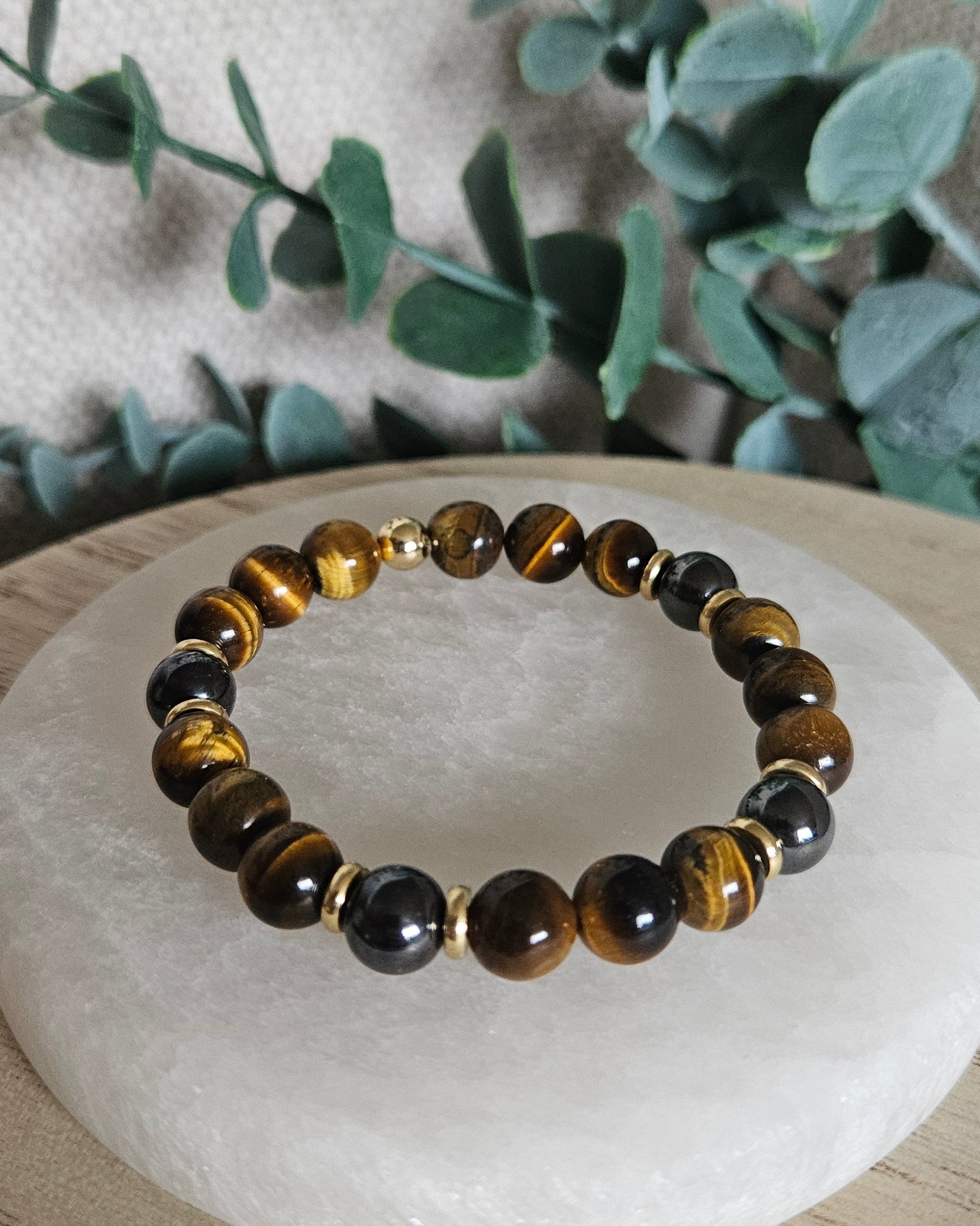 Detailed view of polished Tiger’s Eye and Hematite bracelet beads displayed beside leafy greenery