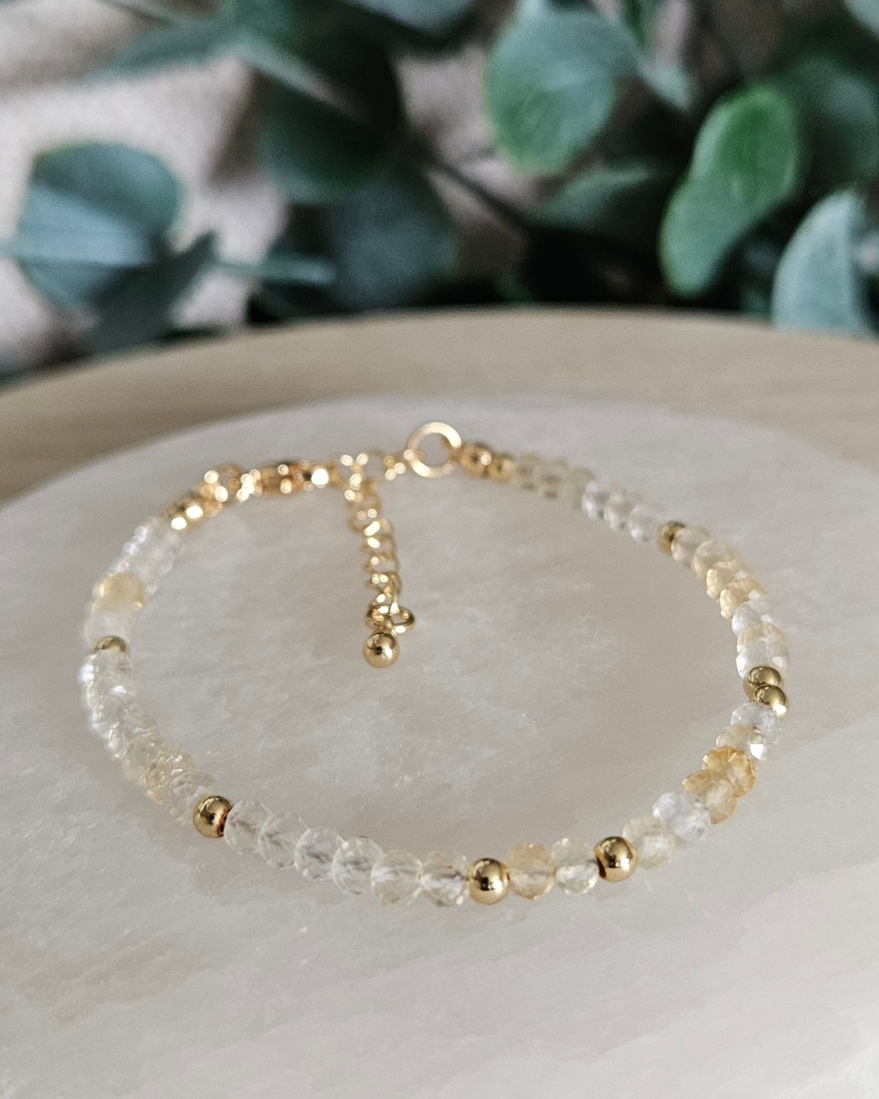 Faceted Citrine rondelle bracelet with gold-plated accents, clasp and extender chain displayed on a round selenite plate
