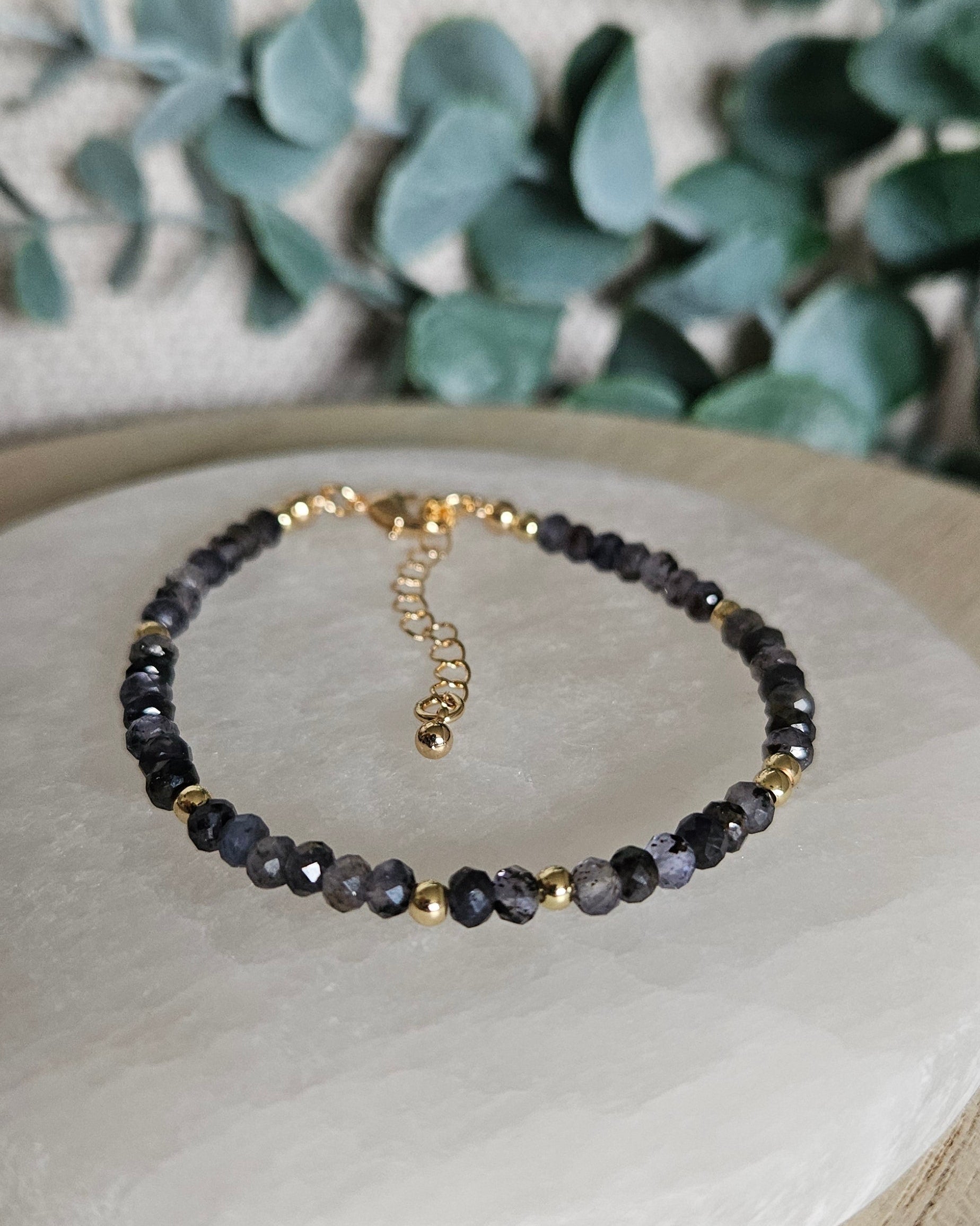 Faceted Iolite bracelet with delicate gold spacers and adjustable clasp displayed on a round selenite plate