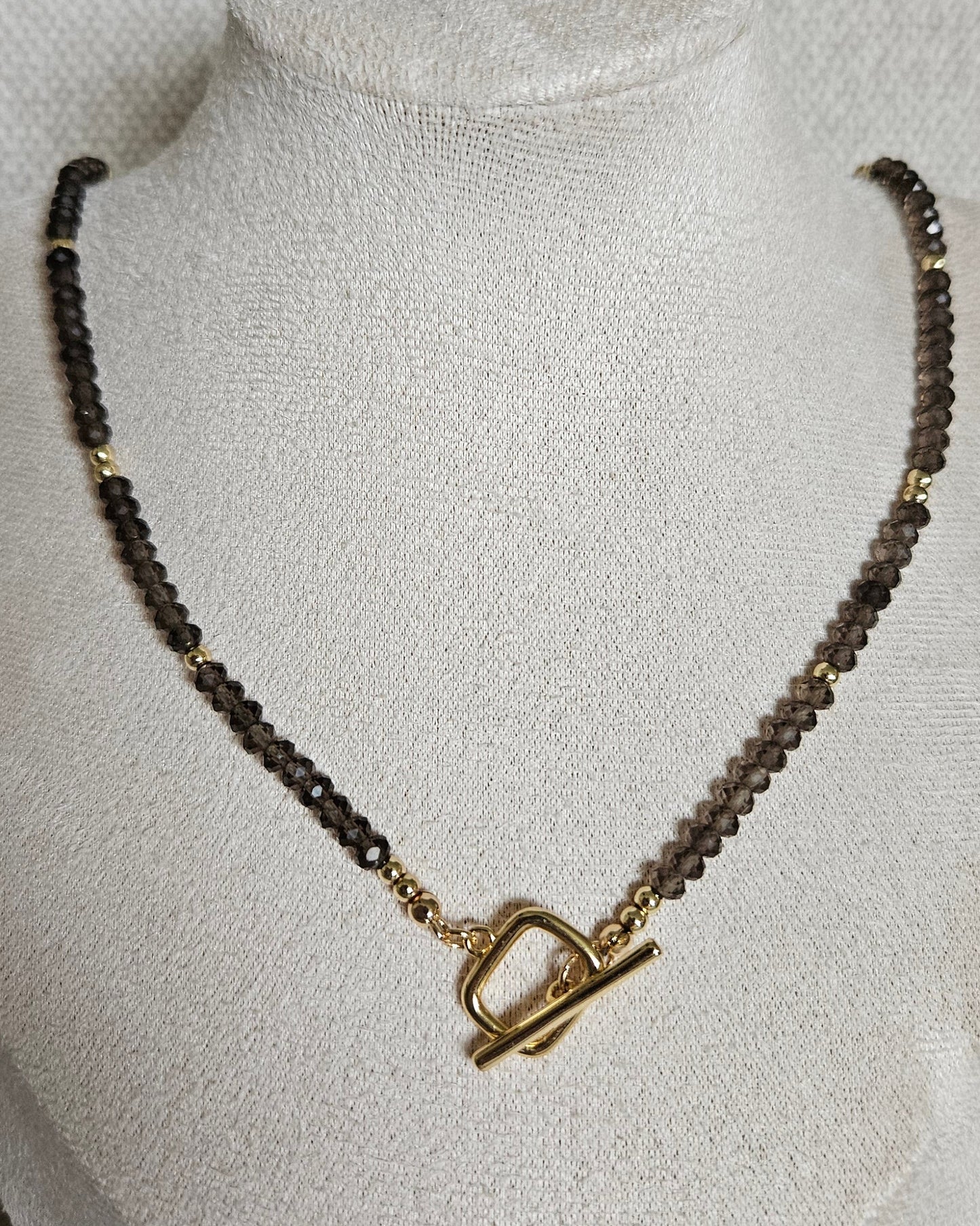 Faceted Smoky Quartz necklace with a gold-plated toggle clasp worn at the front on a beige jewellery bust