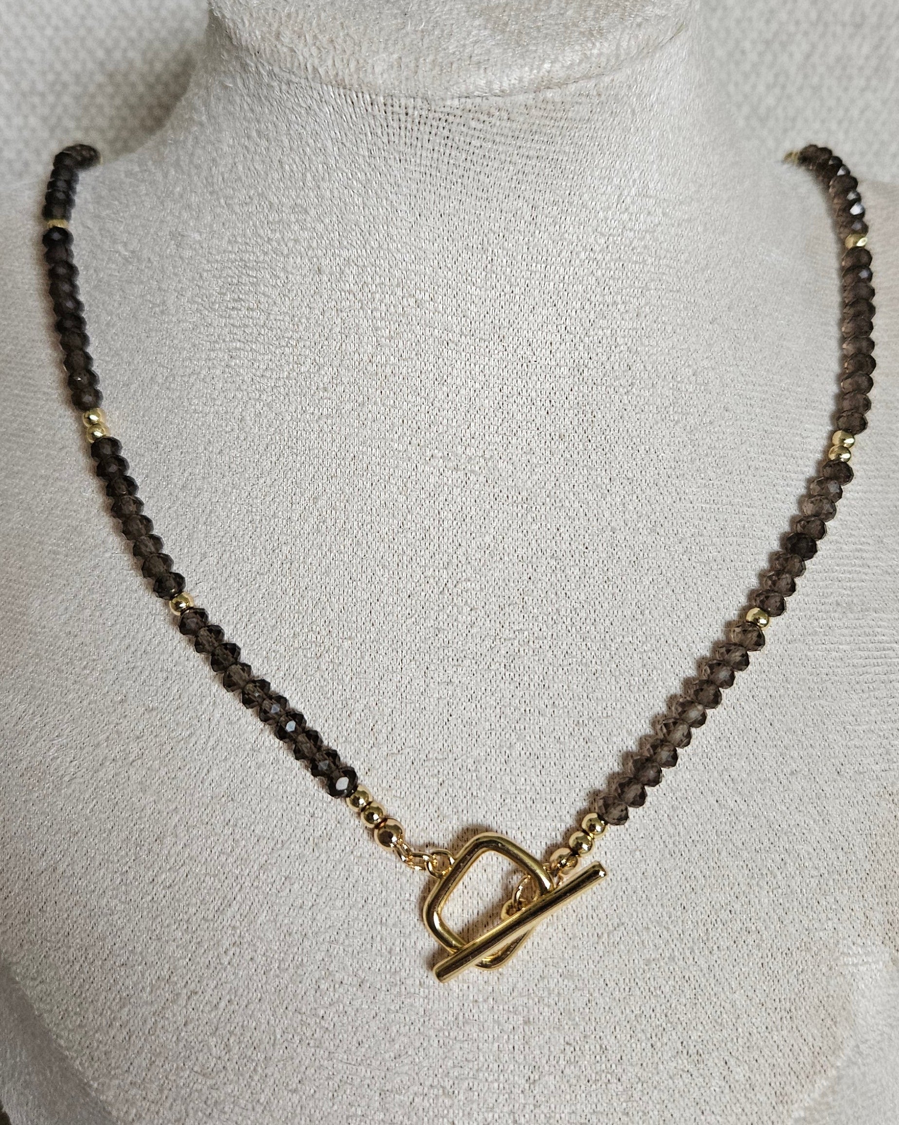 Faceted Smoky Quartz necklace with a gold-plated toggle clasp worn at the front on a beige jewellery bust