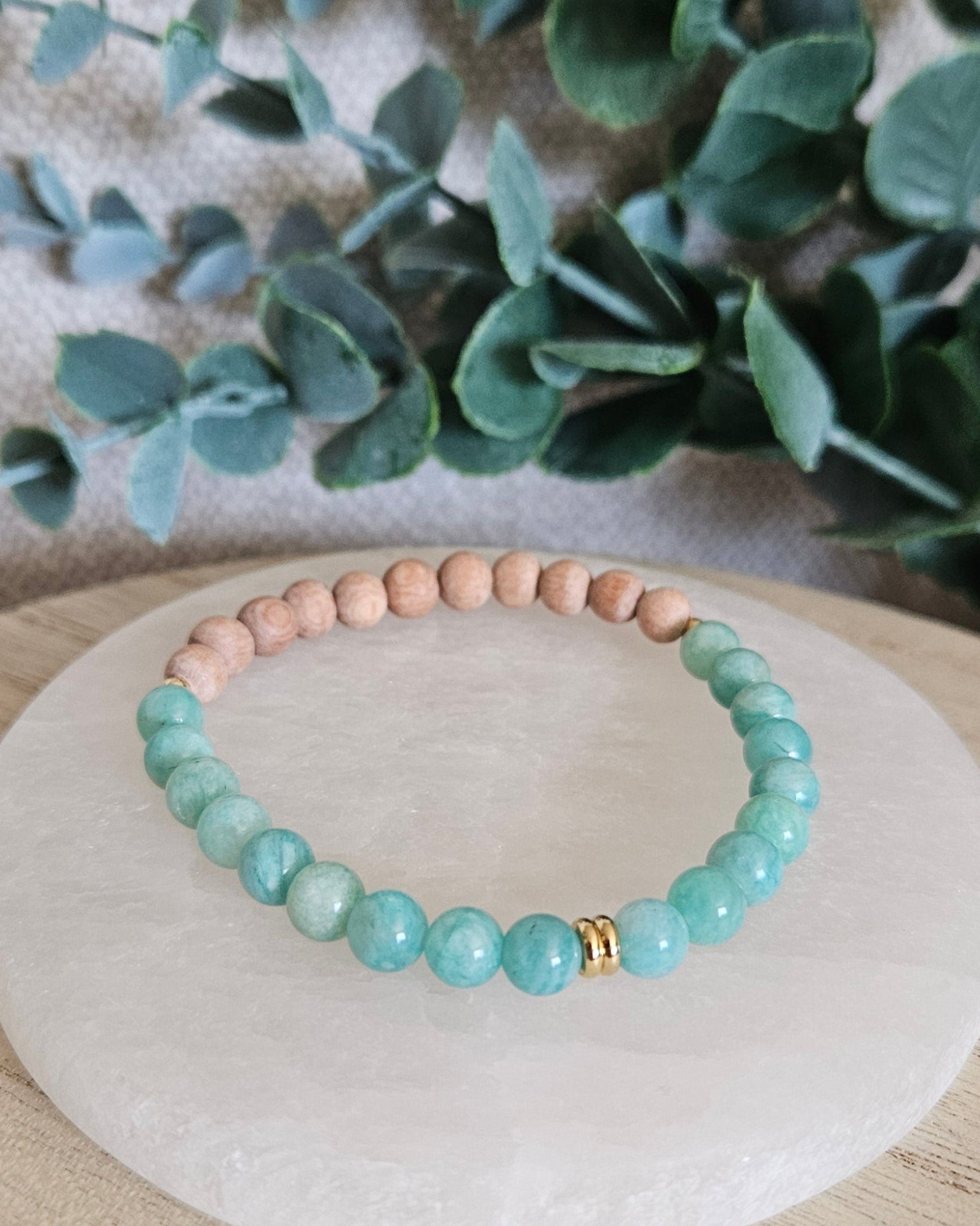 Front view of the blue-green Amazonite and Rosewood stretch bracelet arranged on a round selenite plate