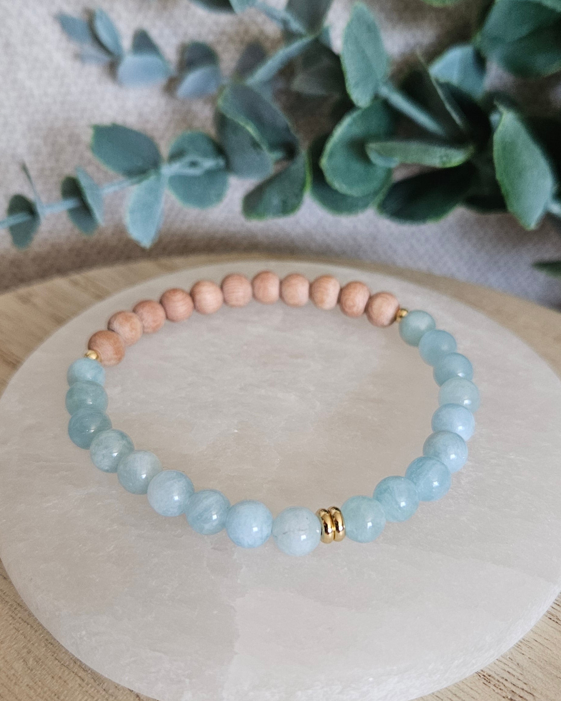 Front view of the pale-blue Aquamarine and Rosewood stretch bracelet arranged on a round selenite plate
