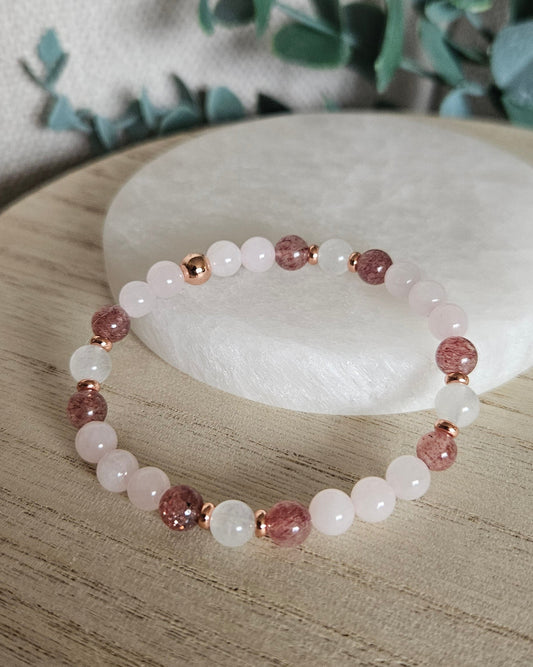 Full Rose Quartz, Moonstone and Strawberry Quartz stretch bracelet with rose gold-plated accents on a wooden surface
